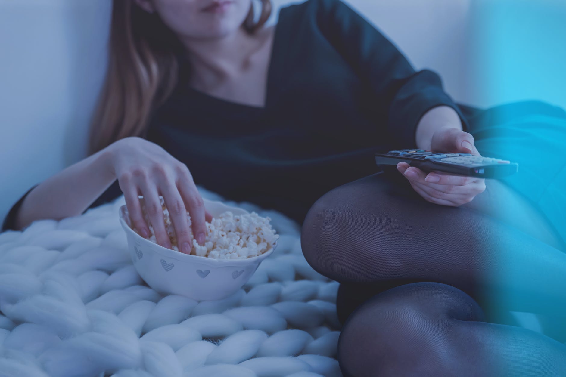 Joven recostada en su cama viendo la televisión con un tazón de palomitas de maíz. | Foto: Pexels