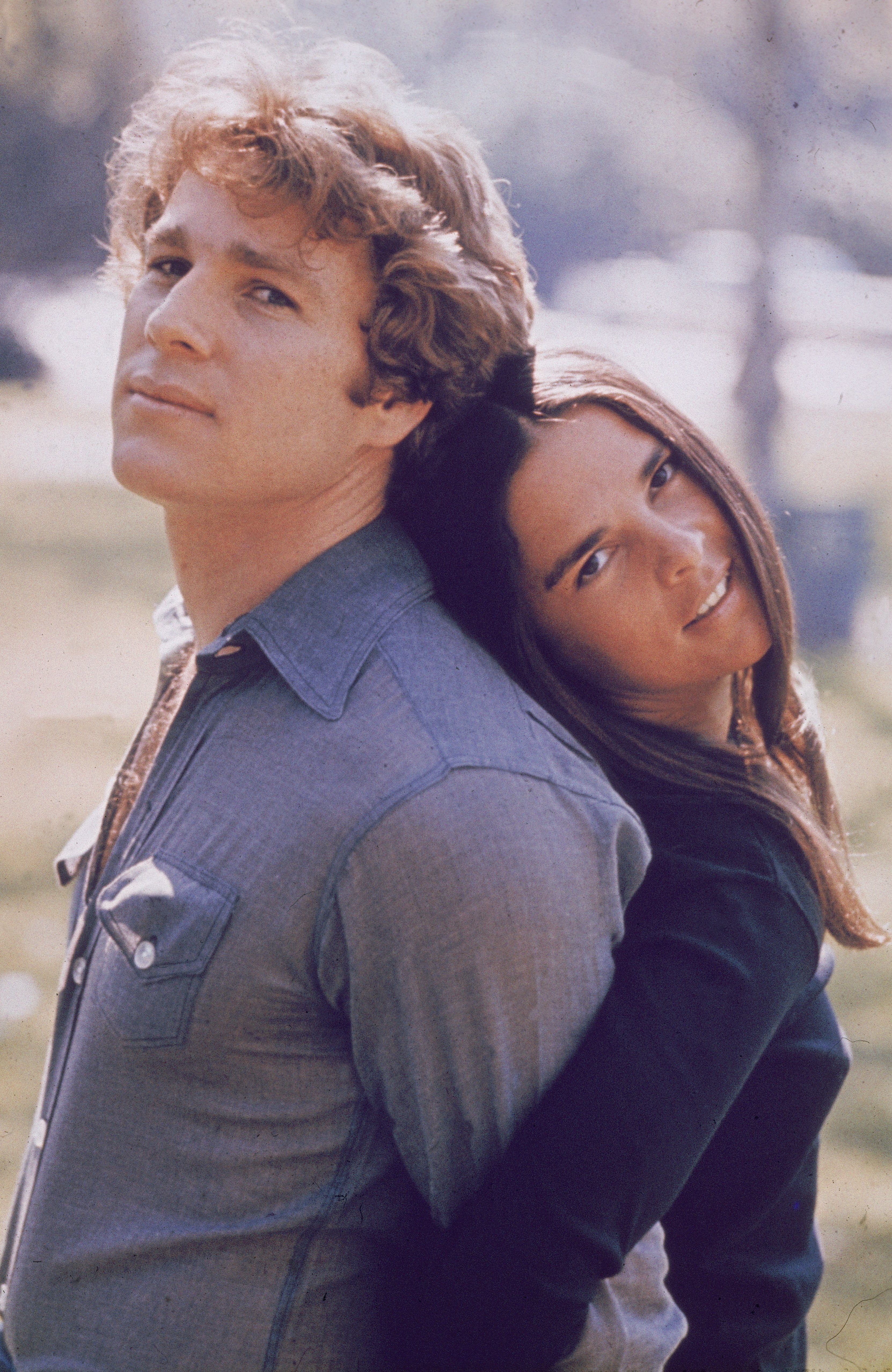 Ryan O'Neal and Ali MacGraw stand back to back outdoors in a still from the 1970 film, "Love Story." | Source: Getty Images