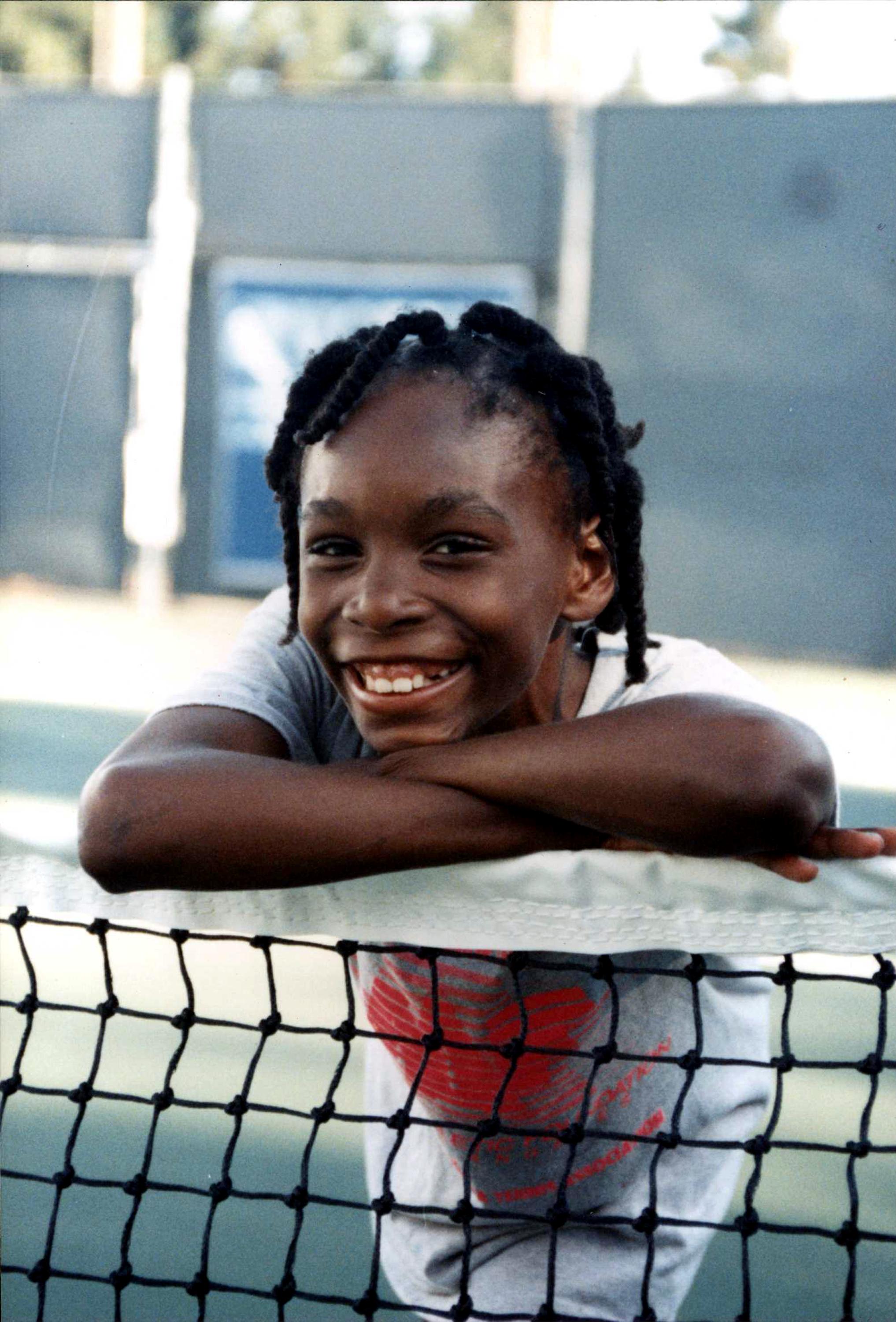 A young Serena Williams beams with joy at the tennis court, full of promise and determination — a glimpse into the early spark that would soon ignite a legendary career.