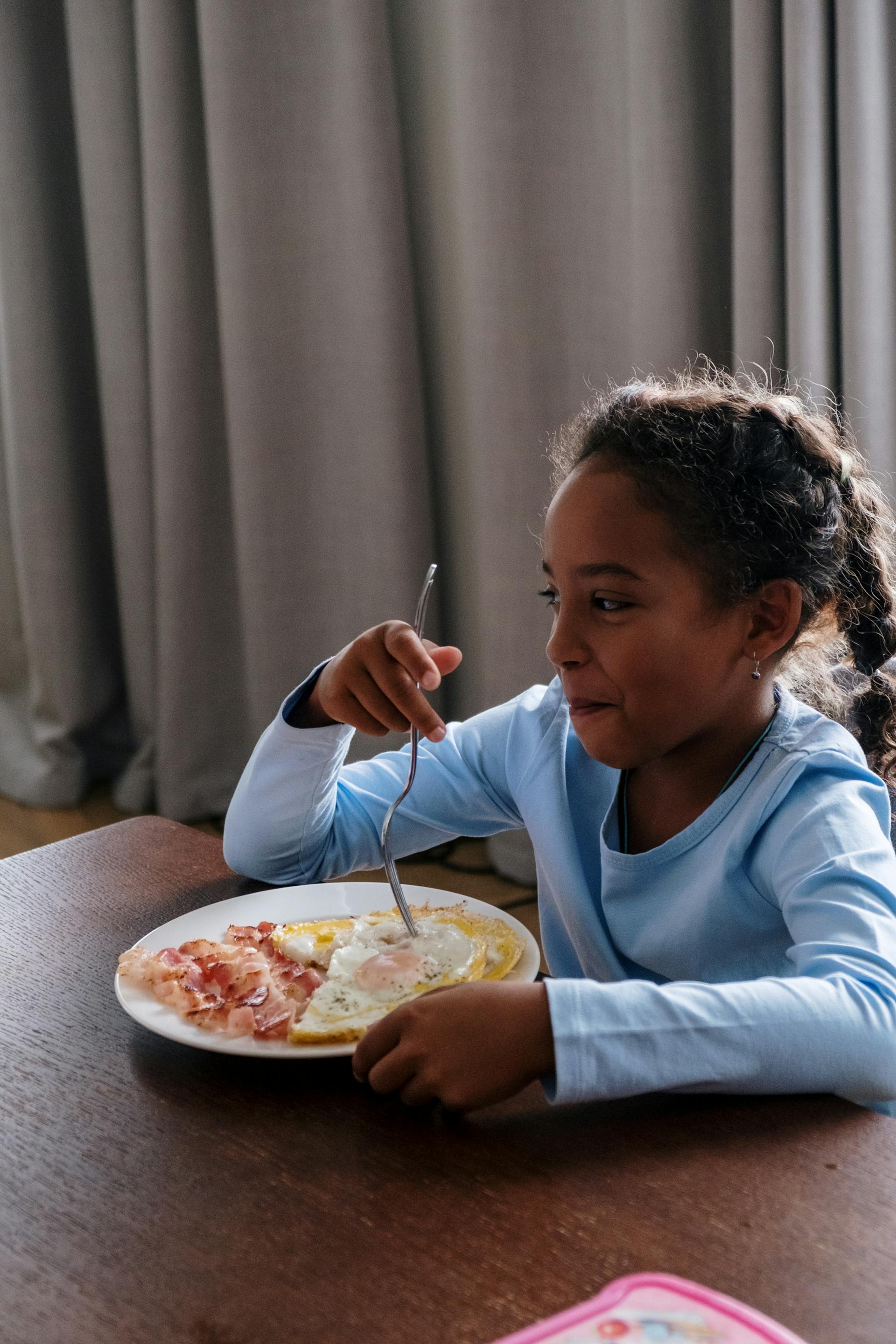 A little girl having breakfast tries to suppress her laughter while looking at someone | Source: Pexels