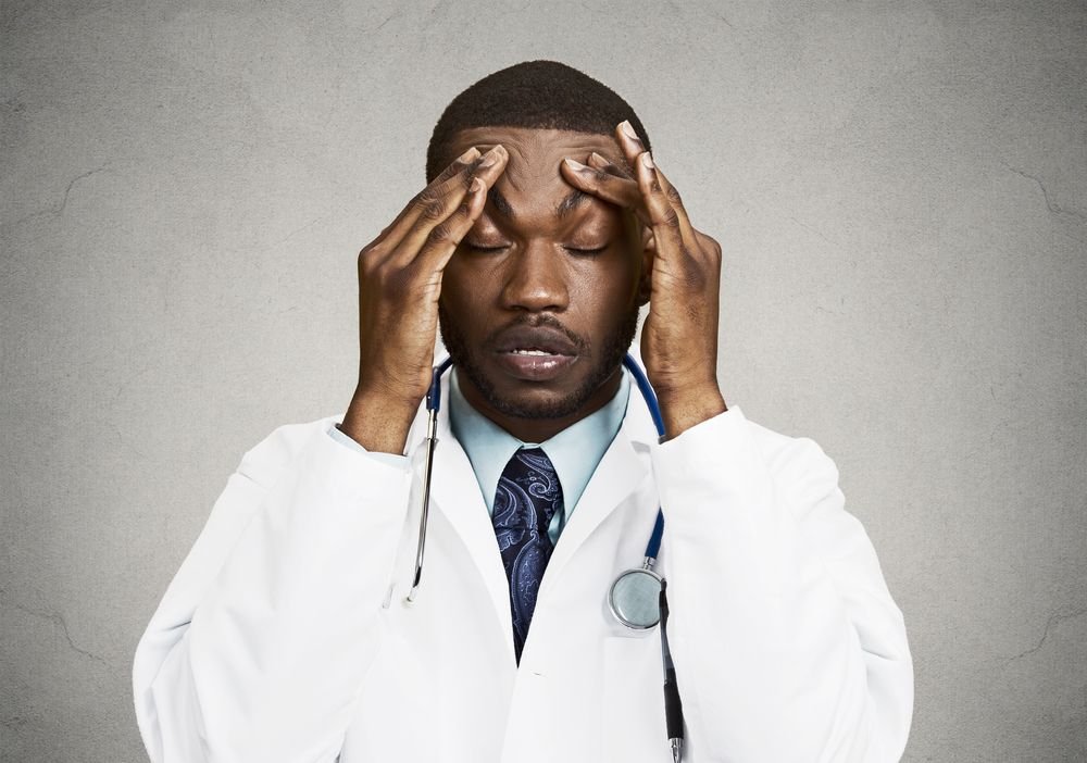 A doctor looks upset while running his temples. | Source: Shutterstock