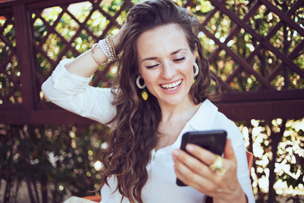A woman smiling while using her phone | Source: Shutterstock