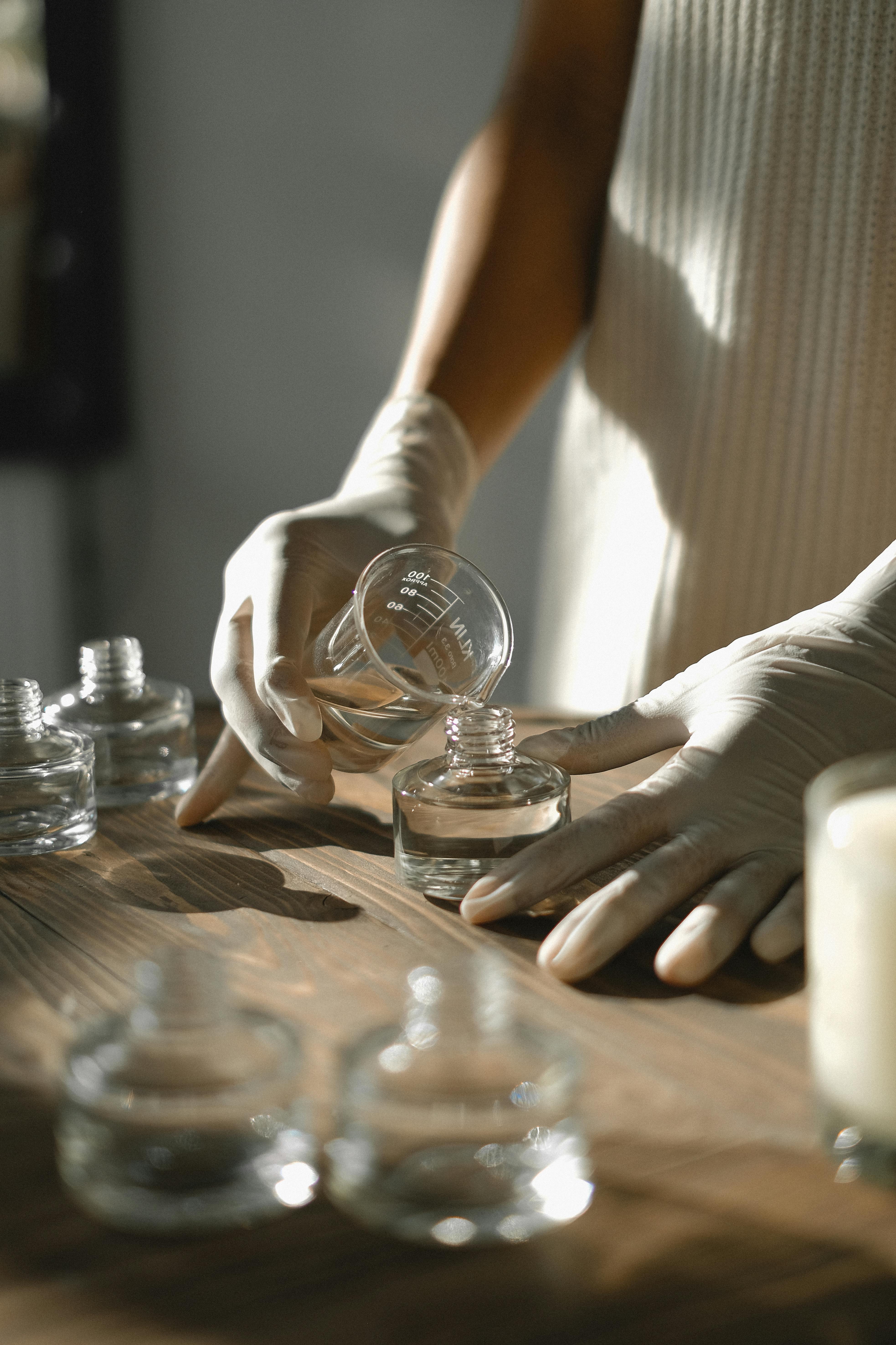 A pair of gloved hands pouring a solution to a bottle of perfume | Source: Pexels