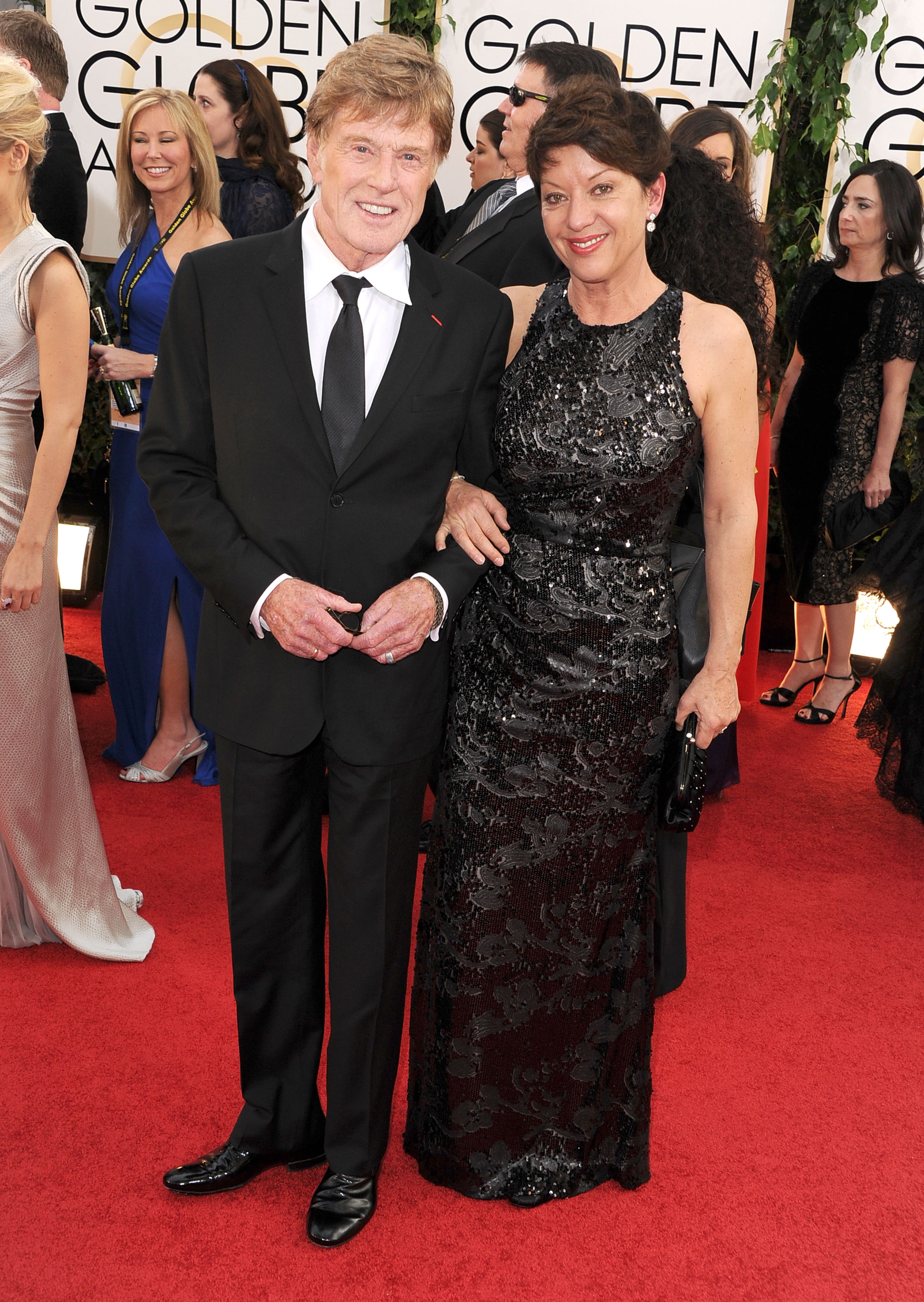 Robert Redford and Sibylle Szaggars arrive at the 71st Annual Golden Globe Awards in Beverly Hills on January 12. Szaggars wears a black floor-length gown with sequined floral details and carries a black clutch. Redford wears a black suit with a white shirt and black tie.