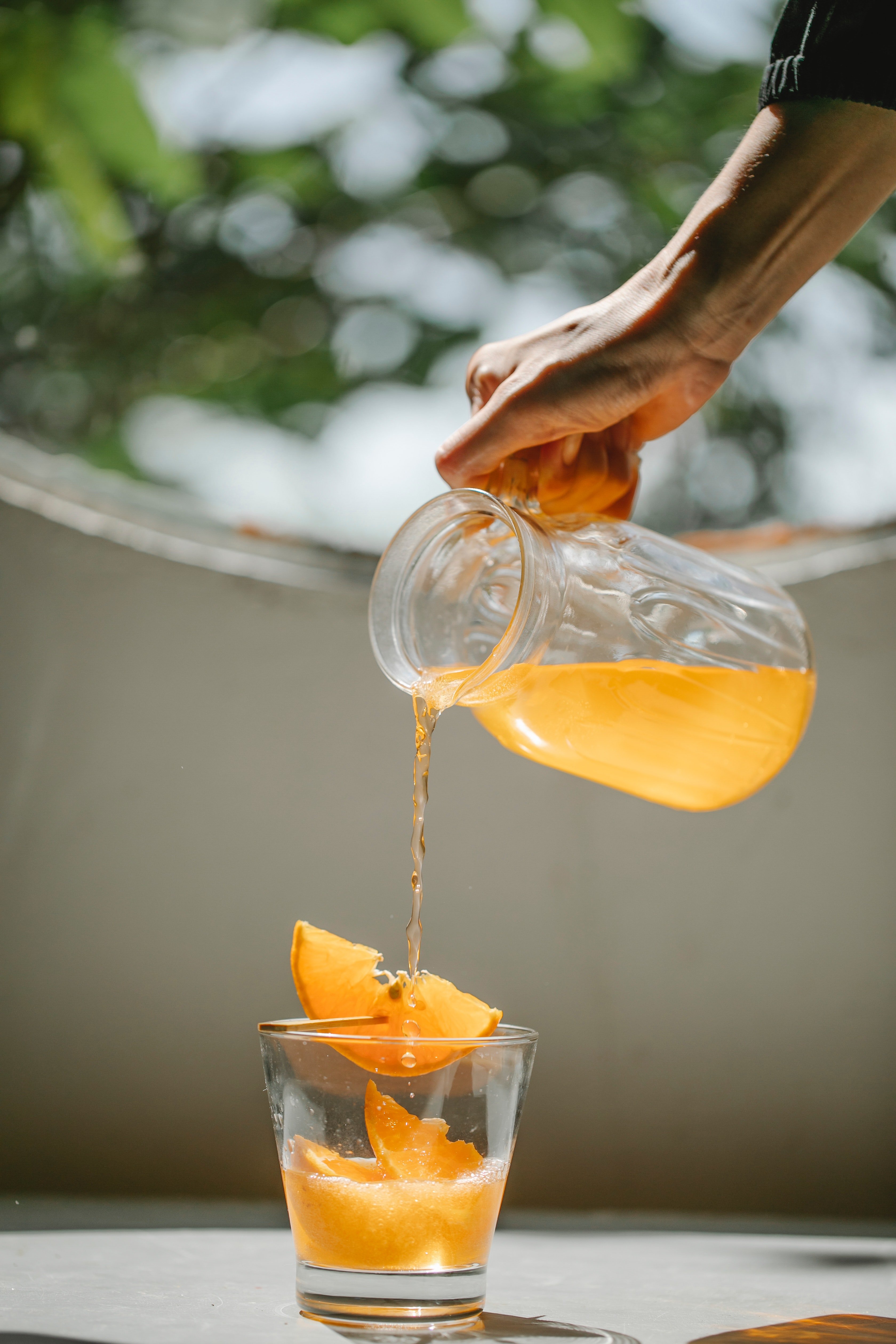 A woman pouring cold orange beverage into glass. | Source: Pexels