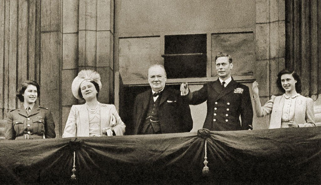 Winston Churchill with Princess Elizabeth, Queen Elizabeth, King George VI, and Princess Margaret, waving from the balcony of Buckingham Palace on VE-Day, 8 May 1945. | Source: Getty Images.