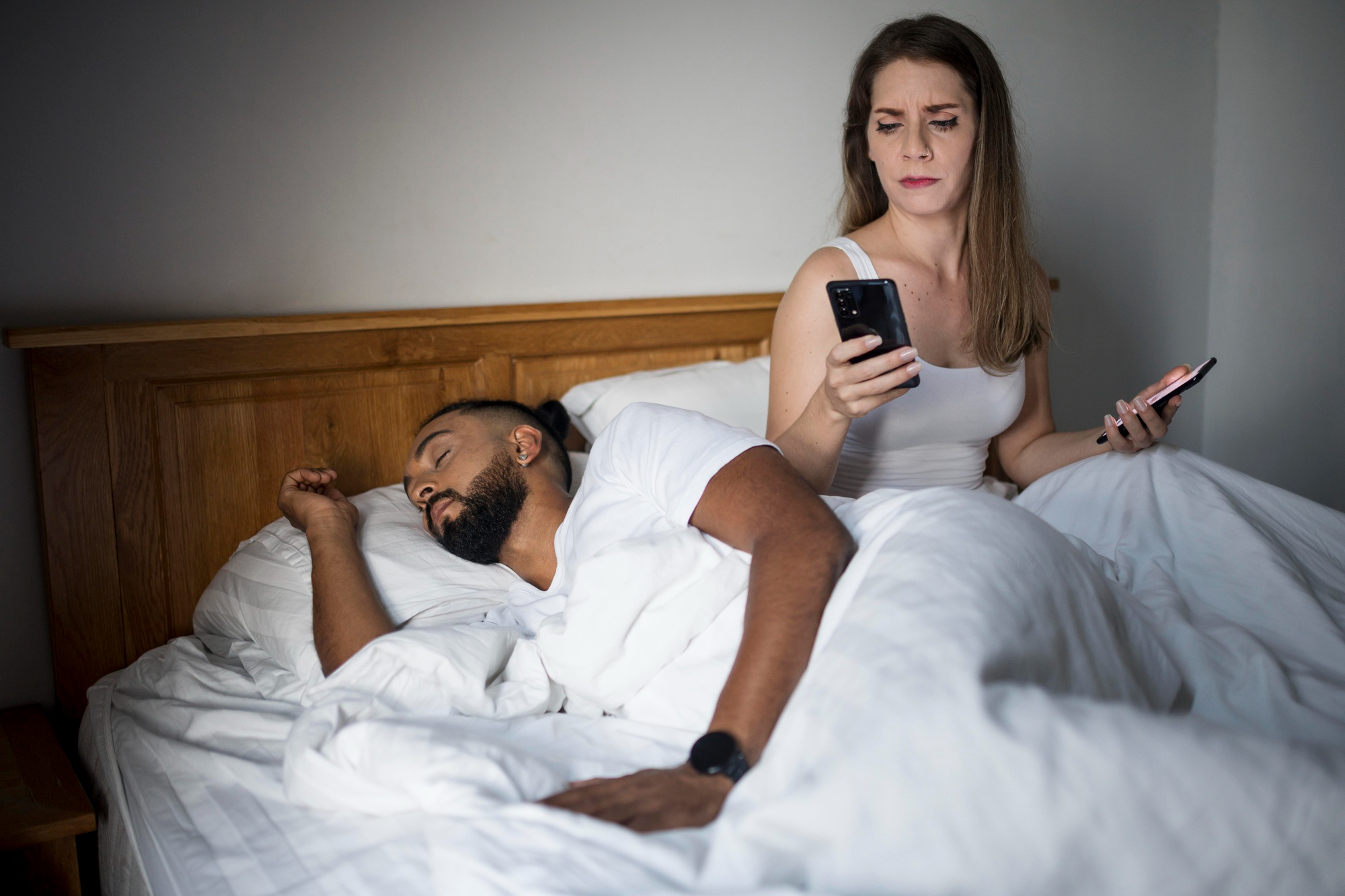 A woman snooping through a man's phone while he's asleep | Source: Freepik