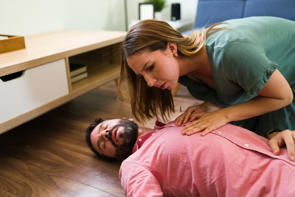 Are you breathing? Attractive young woman checking on a man unconscious on the floor. | Source: Shutterstock