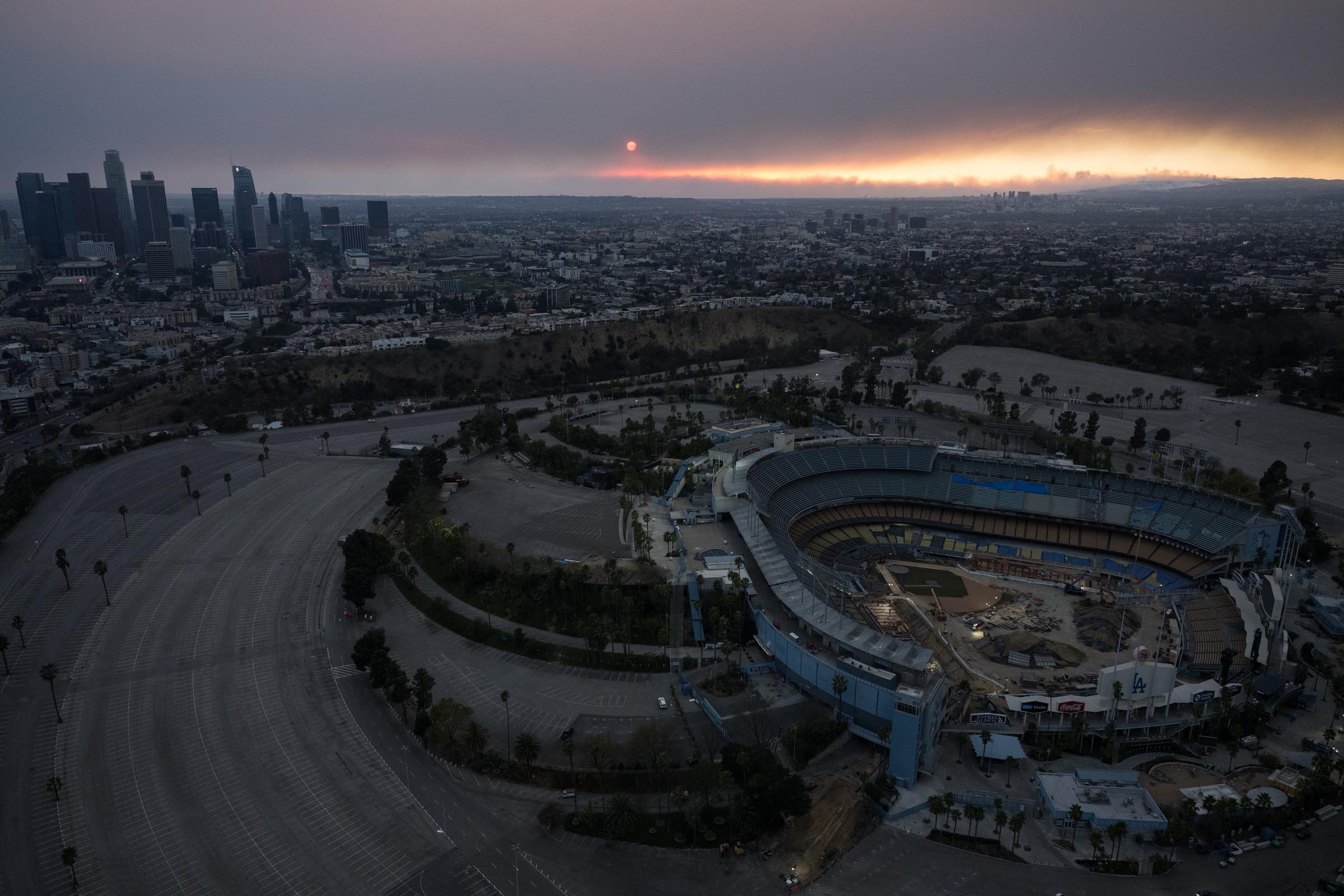 An aerial shot of the sun setting behind the downtown Los Angeles skyline and Dodger Stadium as the sky is engulfed in dark smoke caused by the wildfires in Los Angeles, California on January 8, 2025. | Source: Getty Images