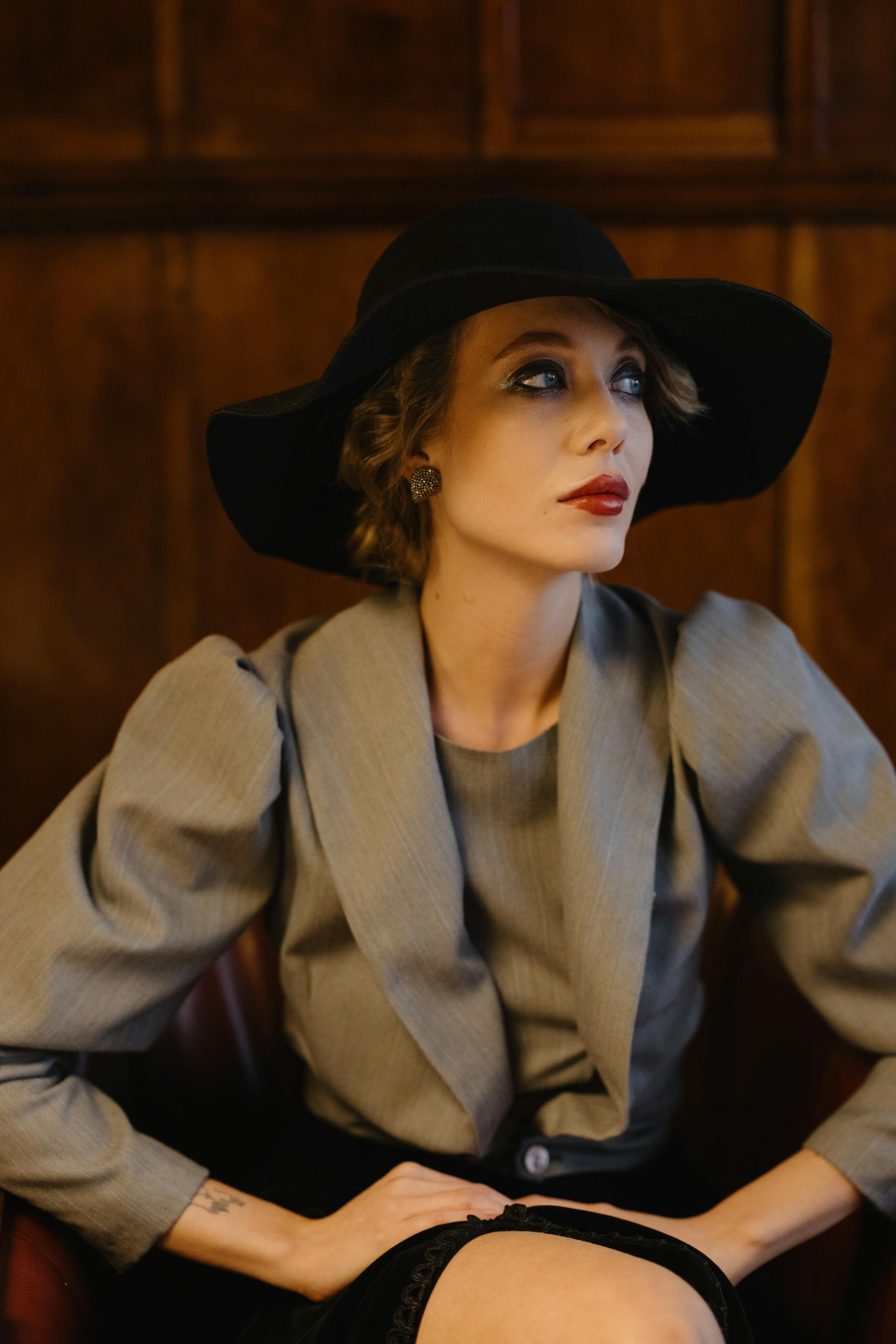 Una mujer elegante con lápiz labial rojo y sombrero negro mira hacia un lado | Fuente: Pexels