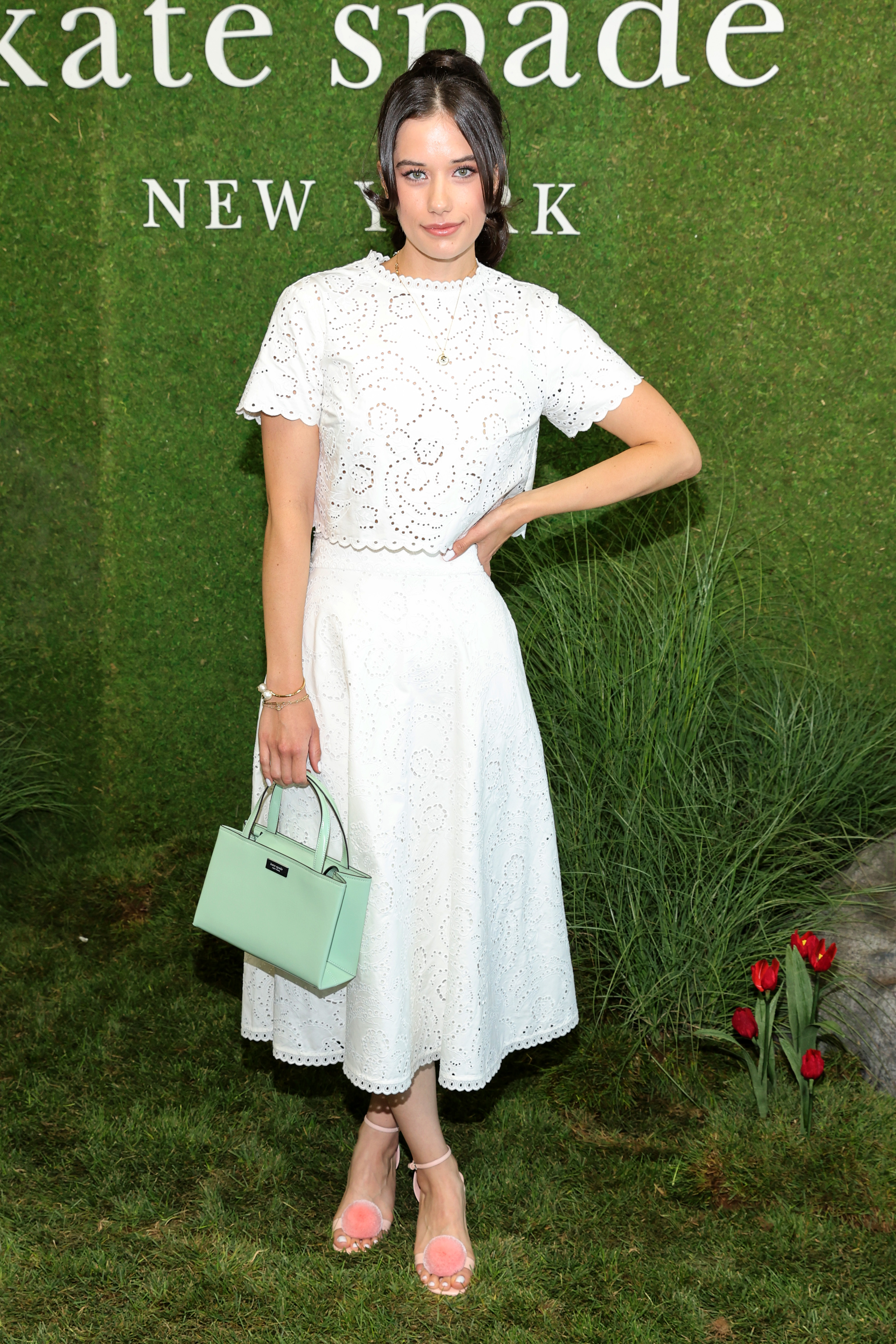 Ella Bleu Travolta poses in a white eyelet dress with a mint handbag at New York Fashion Week in 2022. Her polished appearance at the Kate Spade presentation reflected her growing presence on the fashion scene.