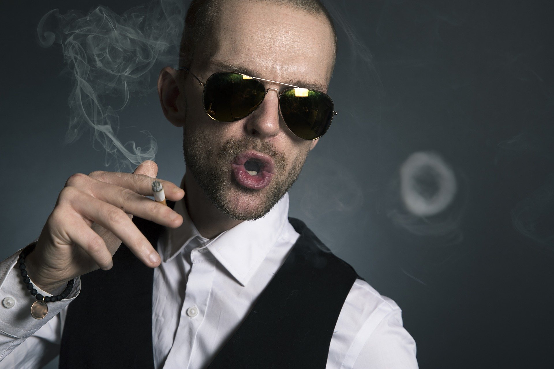 An arrogant rich man wearing sunglasses while blowing out cigarette smoke | Photo: Pixabay/Sammy-Williams