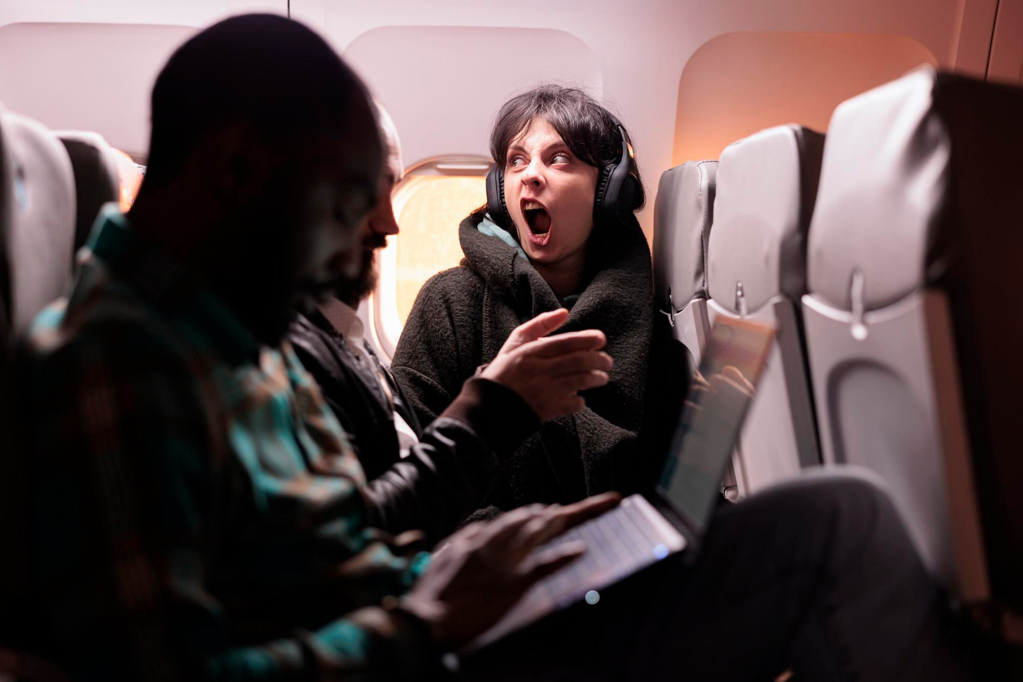 An upset woman wearing headset while screaming on a flight | Source: Freepik