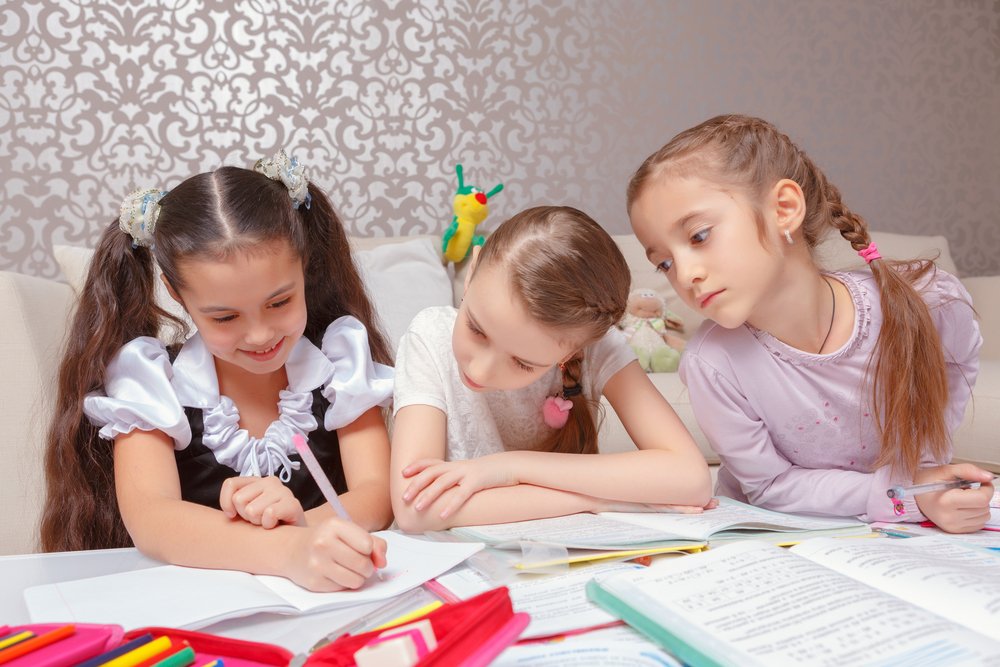Tres niñas haciendo tareas escolares en sus cuadernos desde casa. | Foto: Shutterstock