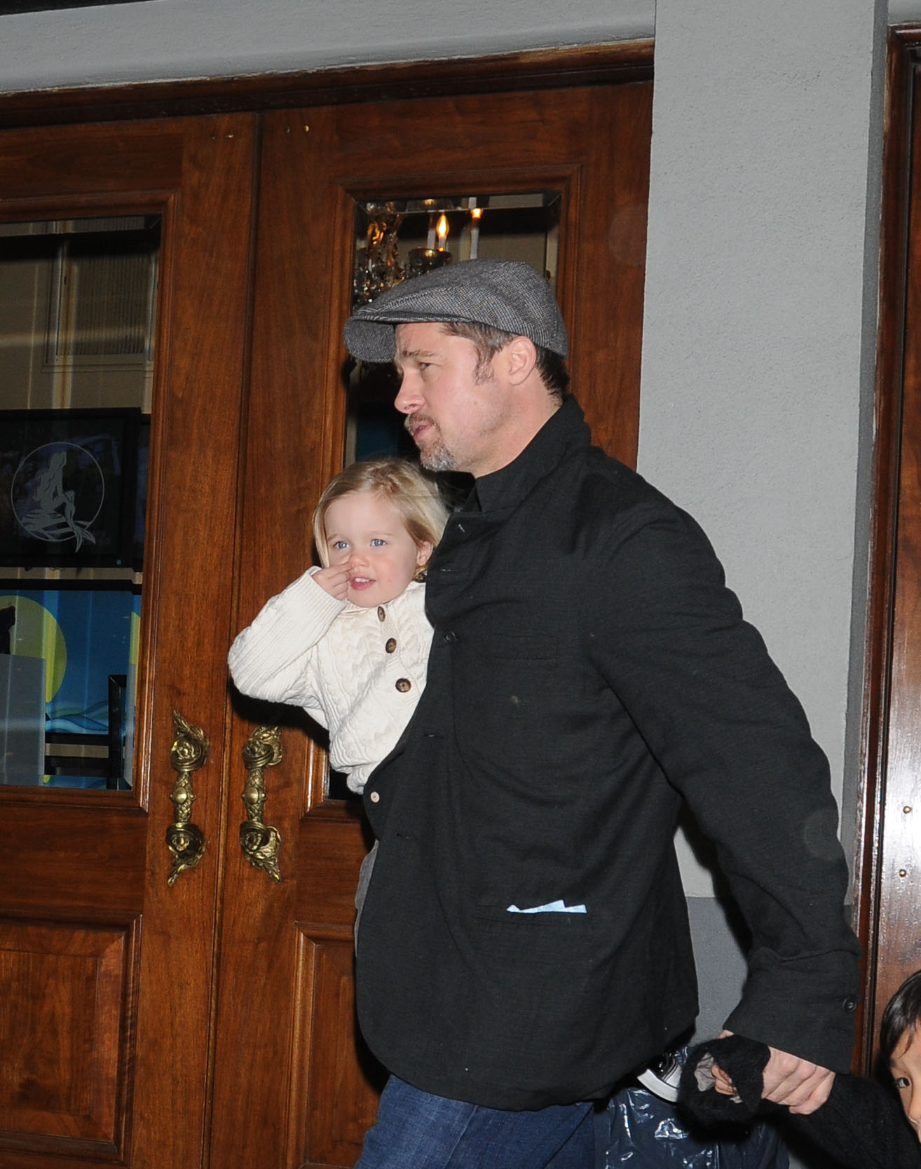 Brad Pitt steps out of a New York City theater carrying Shiloh Jolie-Pitt after "The Little Mermaid" show. Bundled in a cozy sweater, Shiloh rests on his arm, her small hand near her face as she looks ahead. The candid moment captures a quiet, everyday outing with her father.