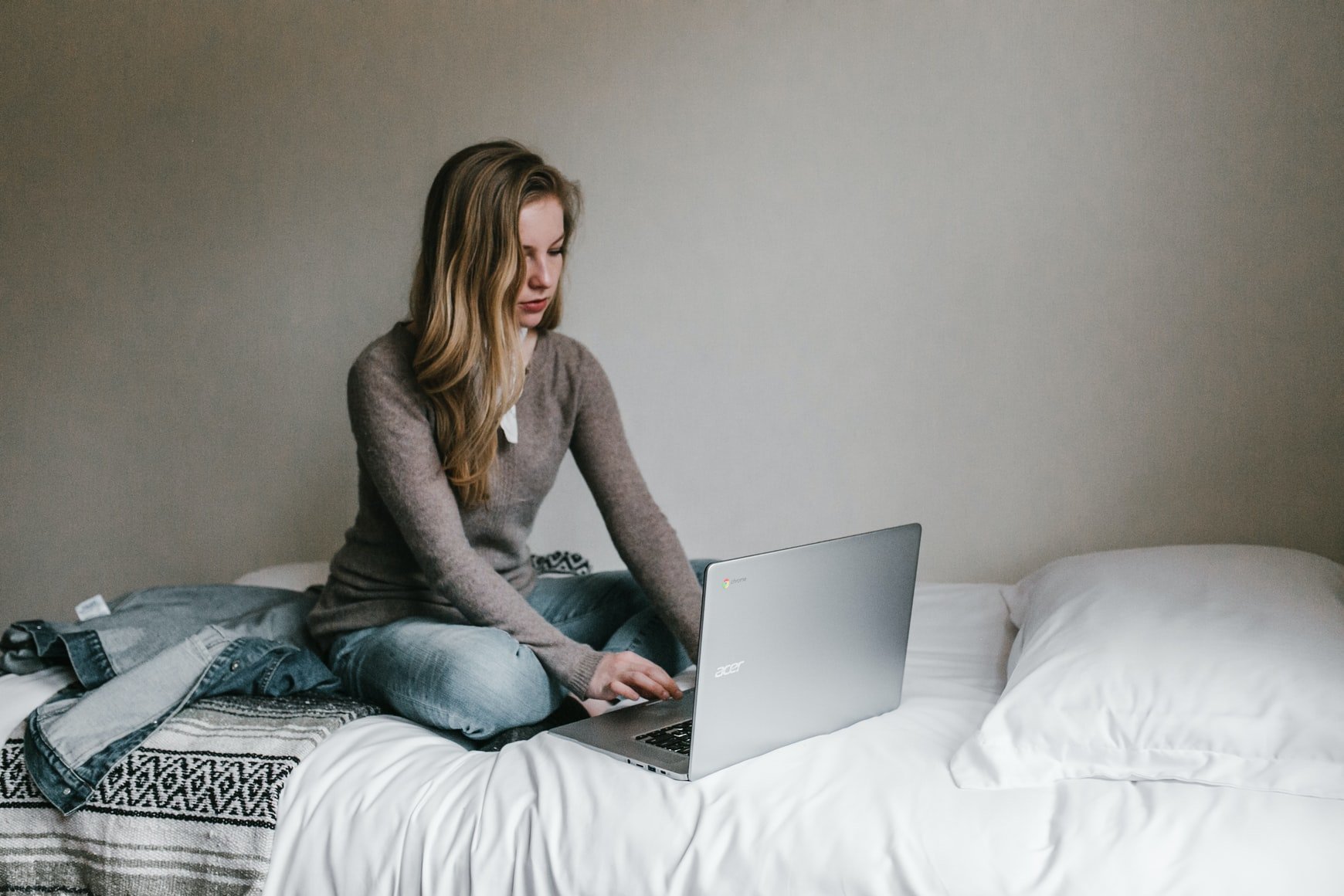 Una mujer usando una computadora portátil mientras está sentada en la cama. | Foto: Unsplash