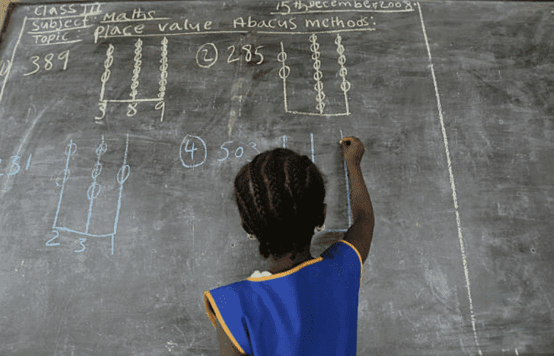 A young girl with braided hair, writing on a school blackboard in Kenema, Sierra Leone | Source: Getty Images (Photo by Ann Johansson/Corbis via Getty Images)