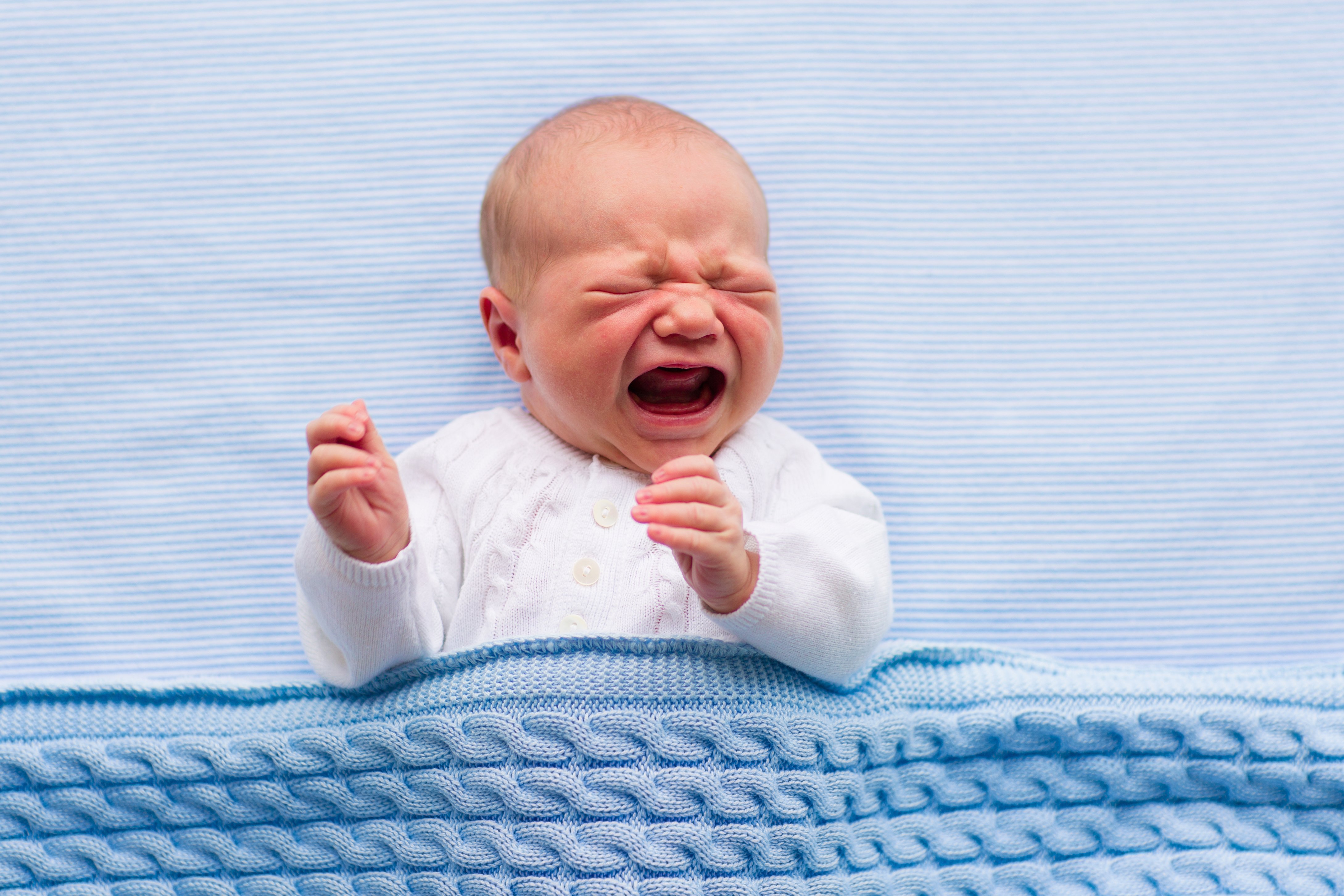 A crying baby under a blue blanket. | Photo: Shutterstock