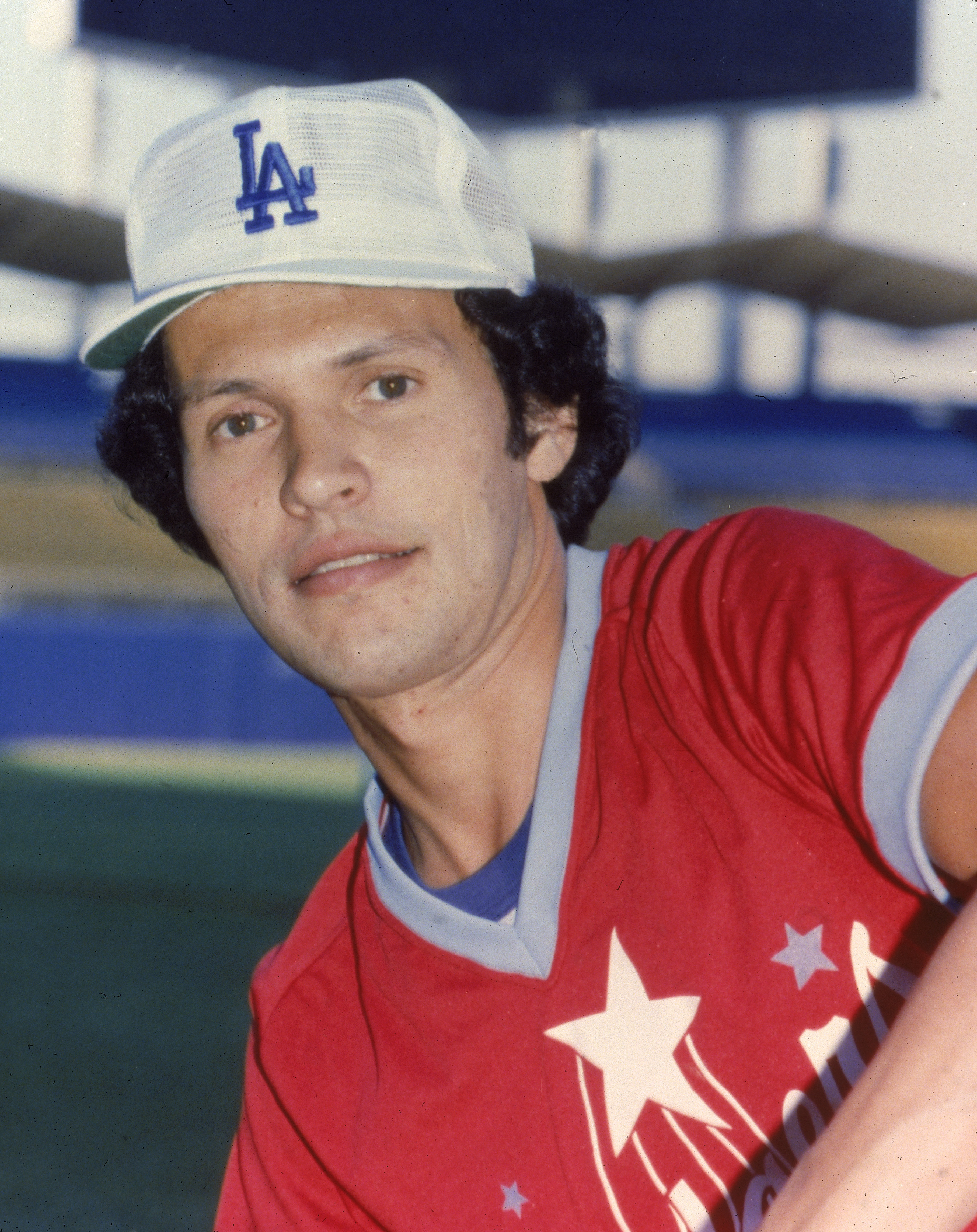American actor and comedian Billy Crystal wears a Los Angeles baseball cap with a red baseball jersey in a sports stadium, 1980. | Source: Getty Images