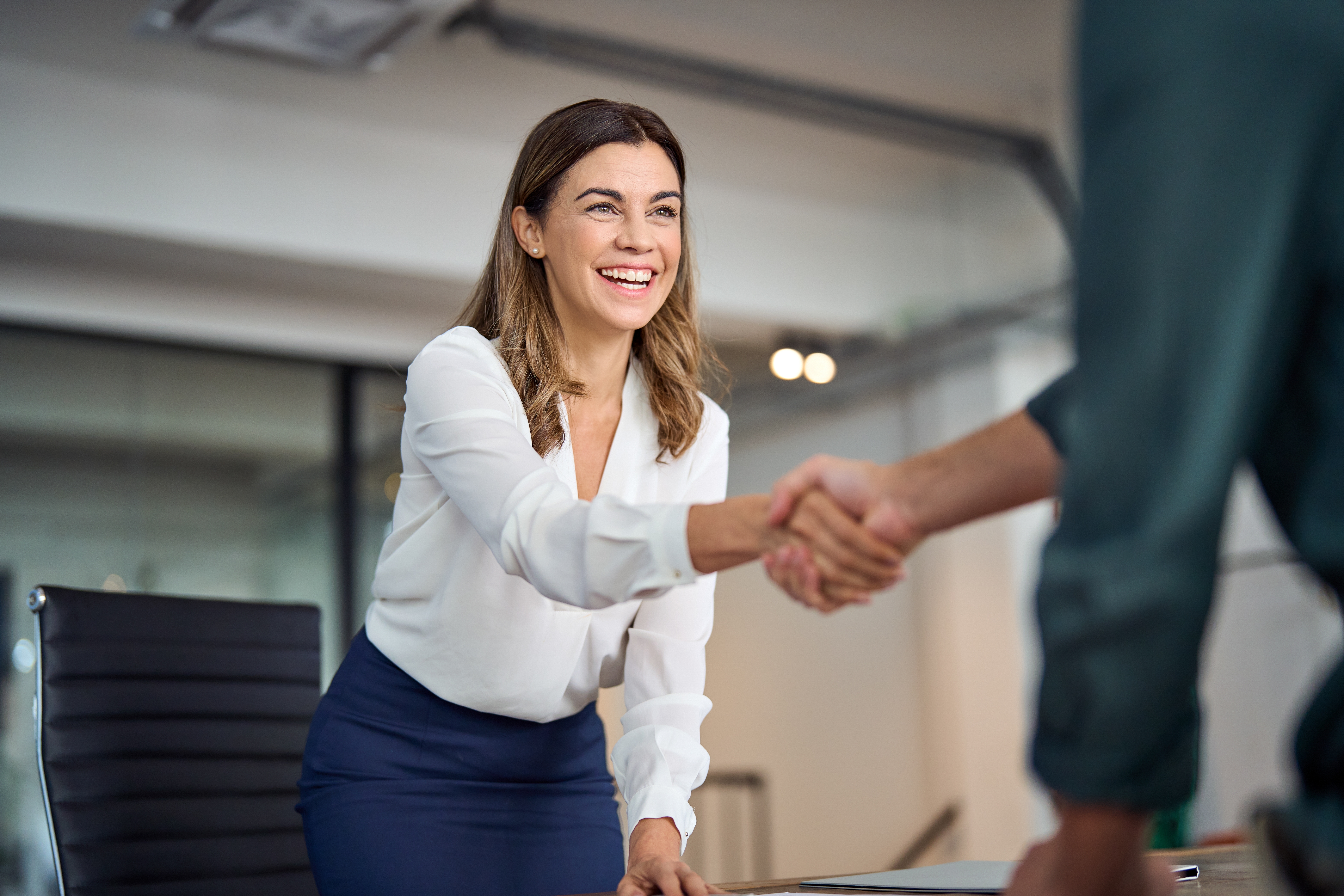 A happy woman shaking hands with a colleague in the office | Source: Shutterstock