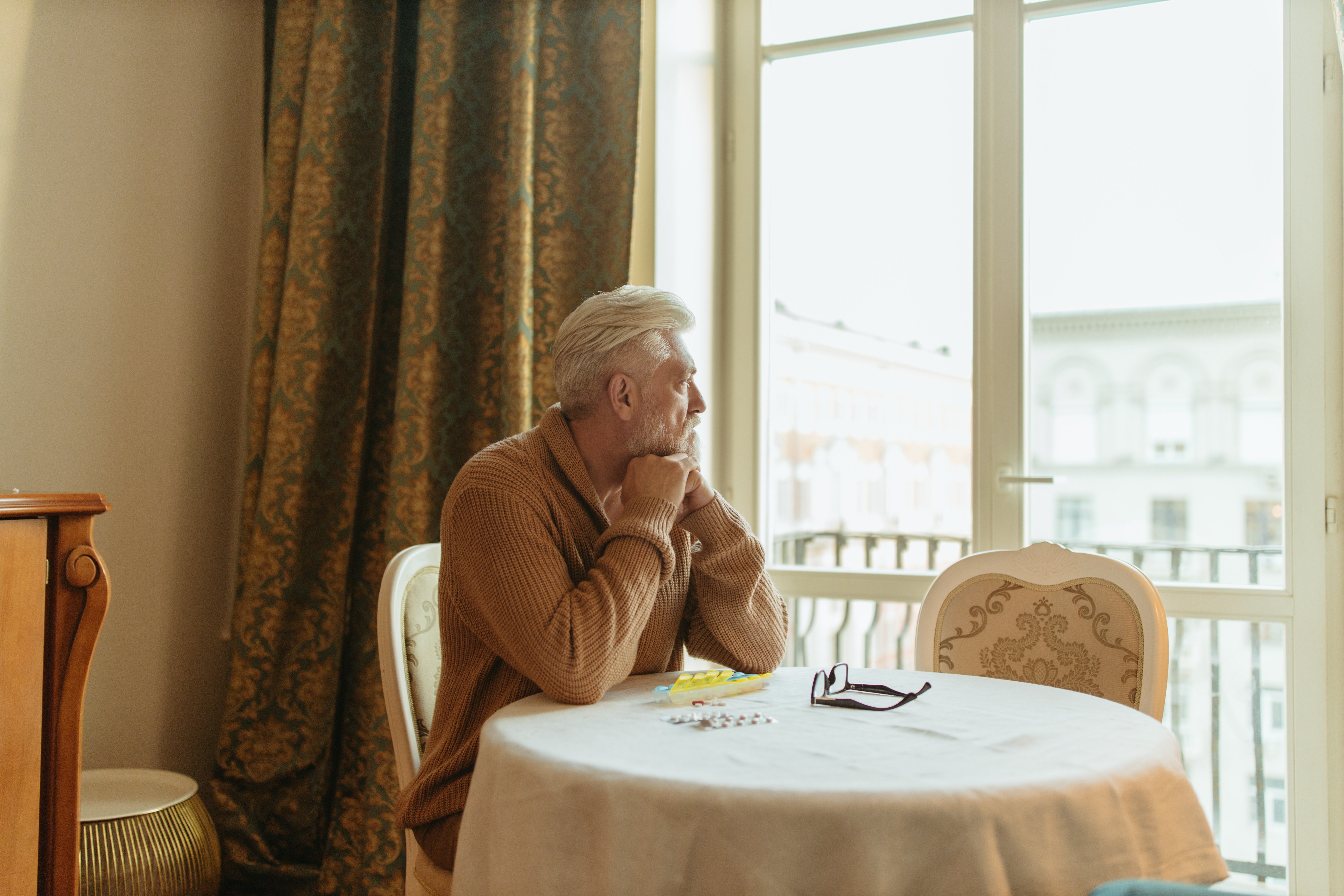 Hombre mayor mira distraidamente por un ventanal. | Foto: Pexels