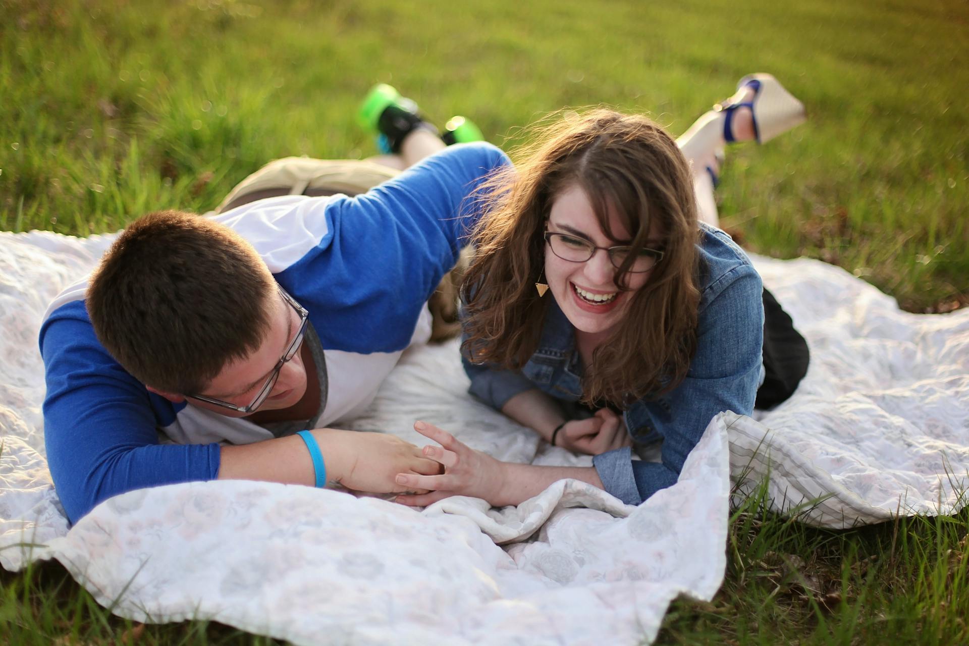 A man and a woman laugh while lying on a mat on the grass | Source: Pexels