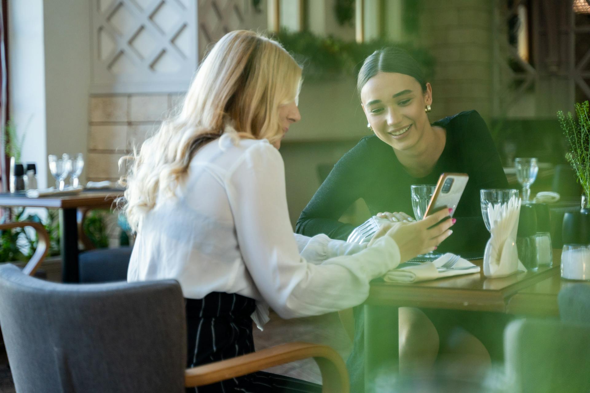 Two women smiling while looking at a phone screen in a restaurant | Source: Pexels