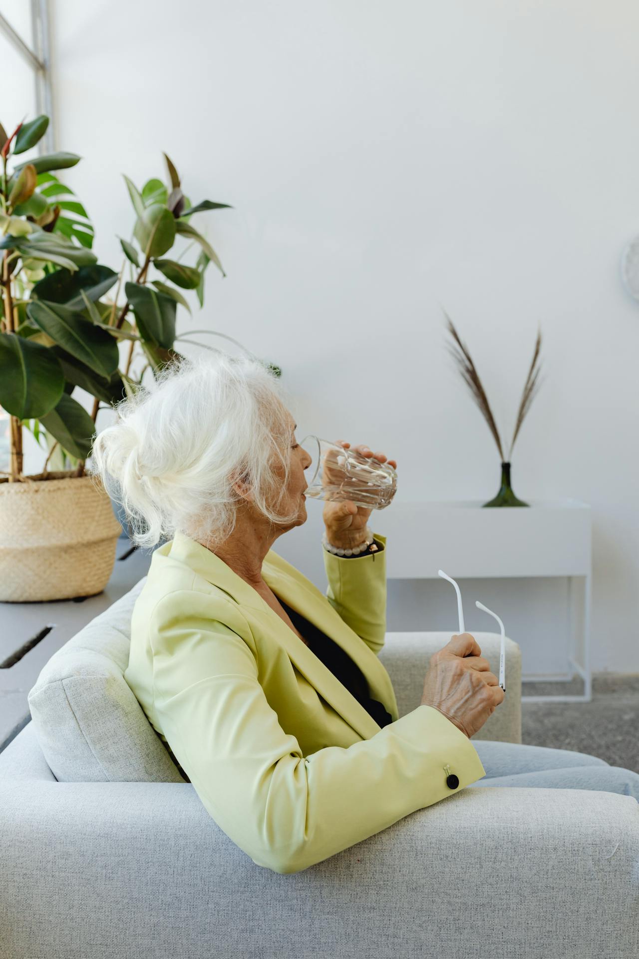 A senior woman sitting on the couch and drinking a glass of water | Source: Pexels