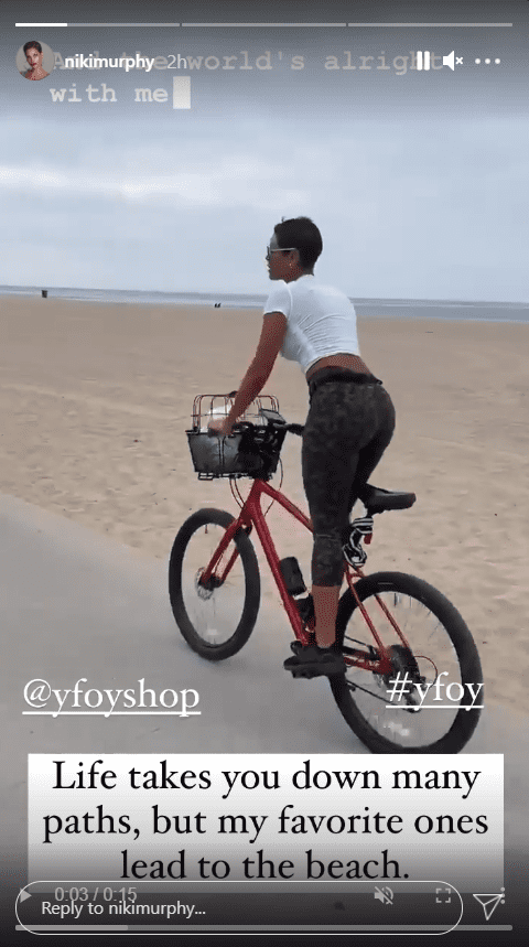 A screenshot of Nicole Murphy in a white T-shirt cycling while on the beach | Photo: Instagram/nikimurphy