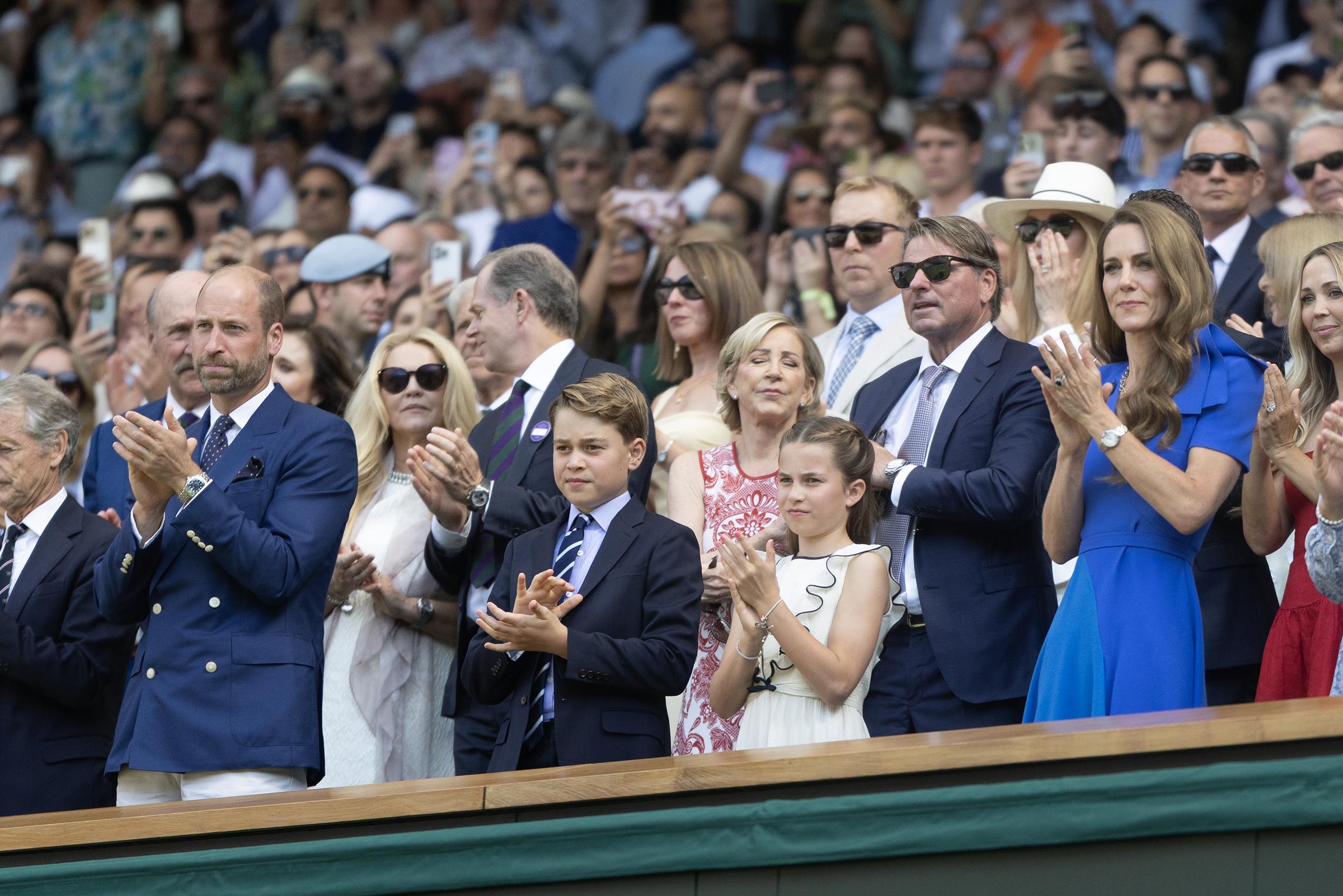 The Prince and Princess of Wales stand and applaud in the Royal Box with their children, Prince George and Princess Charlotte. All four appear composed as they observe the final moments of the match.