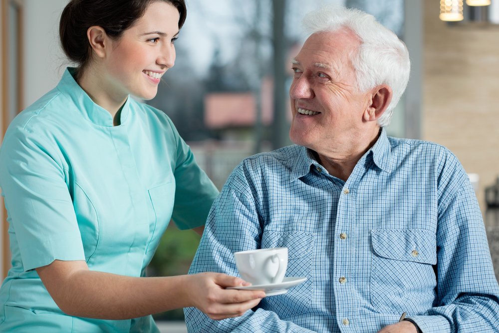 Cuidadora sirviéndole una taza de café a un anciano sonriente. | Fuente: Shutterstock