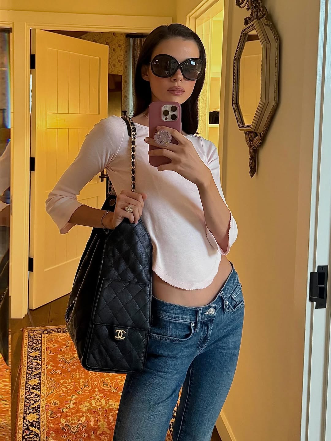 Striking a pose for a mirror selfie with ease, Nicola blends casual cool with understated luxury. She pairs a pale pink fitted top with classic denim, accessorized with oversized sunglasses and a quilted black handbag for a crisp, laid-back finish. | Source: Instagram/nicolapeltzbeckham