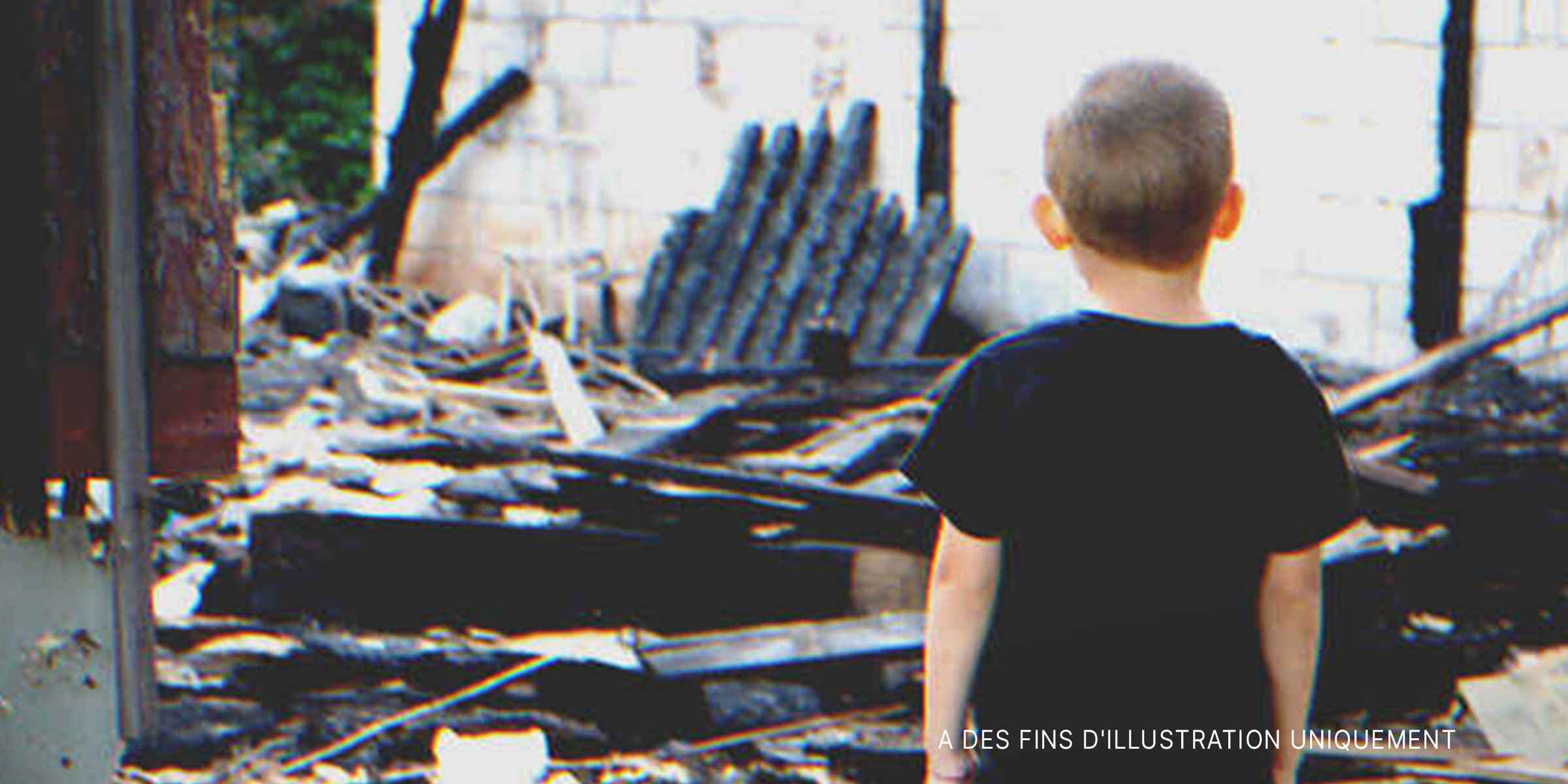 Un garçon regarde les restes d'une maison incendiée | Source : Shutterstock