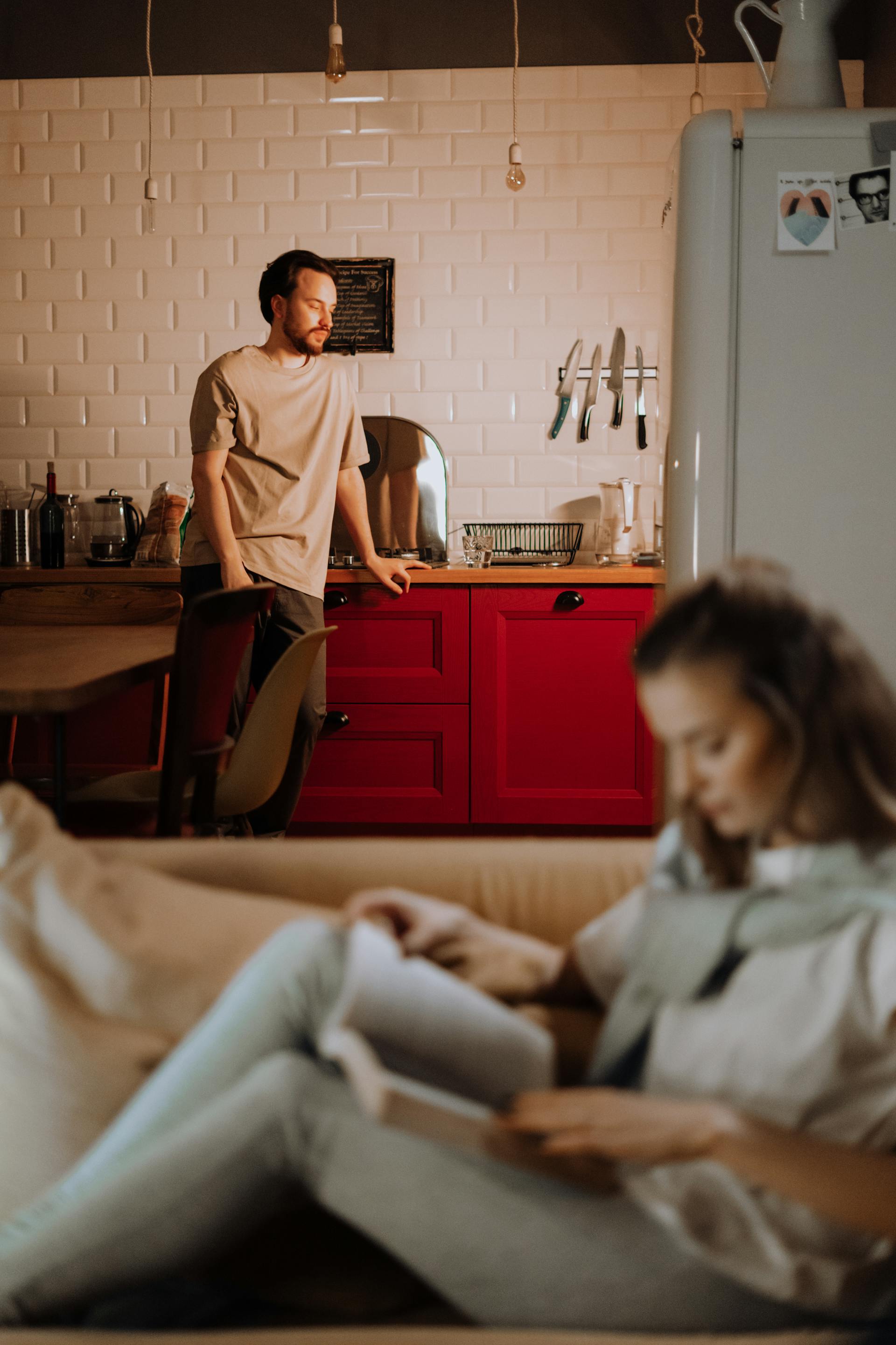 A woman reading a book on the couch while a distressed man is standing in the kitchen | Source: Pexels