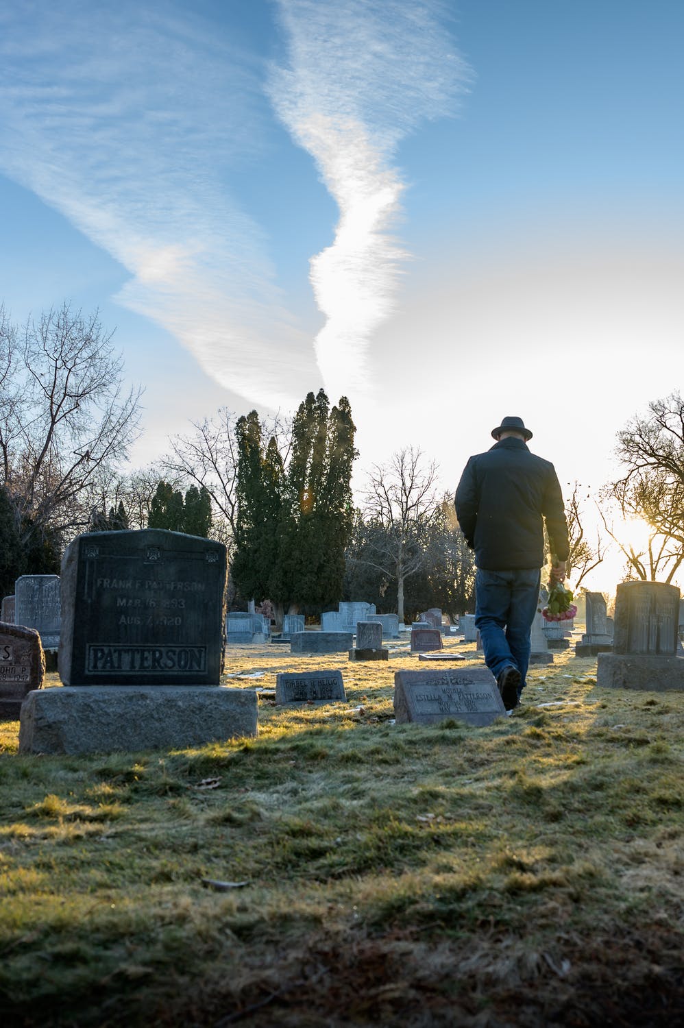 Hombre caminando en un cementerio con flores en la mano. | Foto: Pexels
