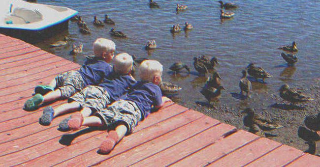 Three kids looking at a bunch of ducks in a lake | Source: Shutterstock