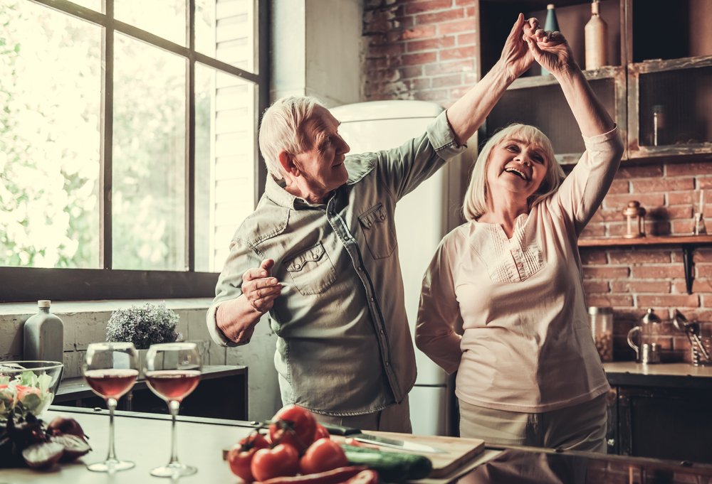 A photo of a senior couple dancing and smiling while cooking together in kitchen. | Photo: Shutterstock.