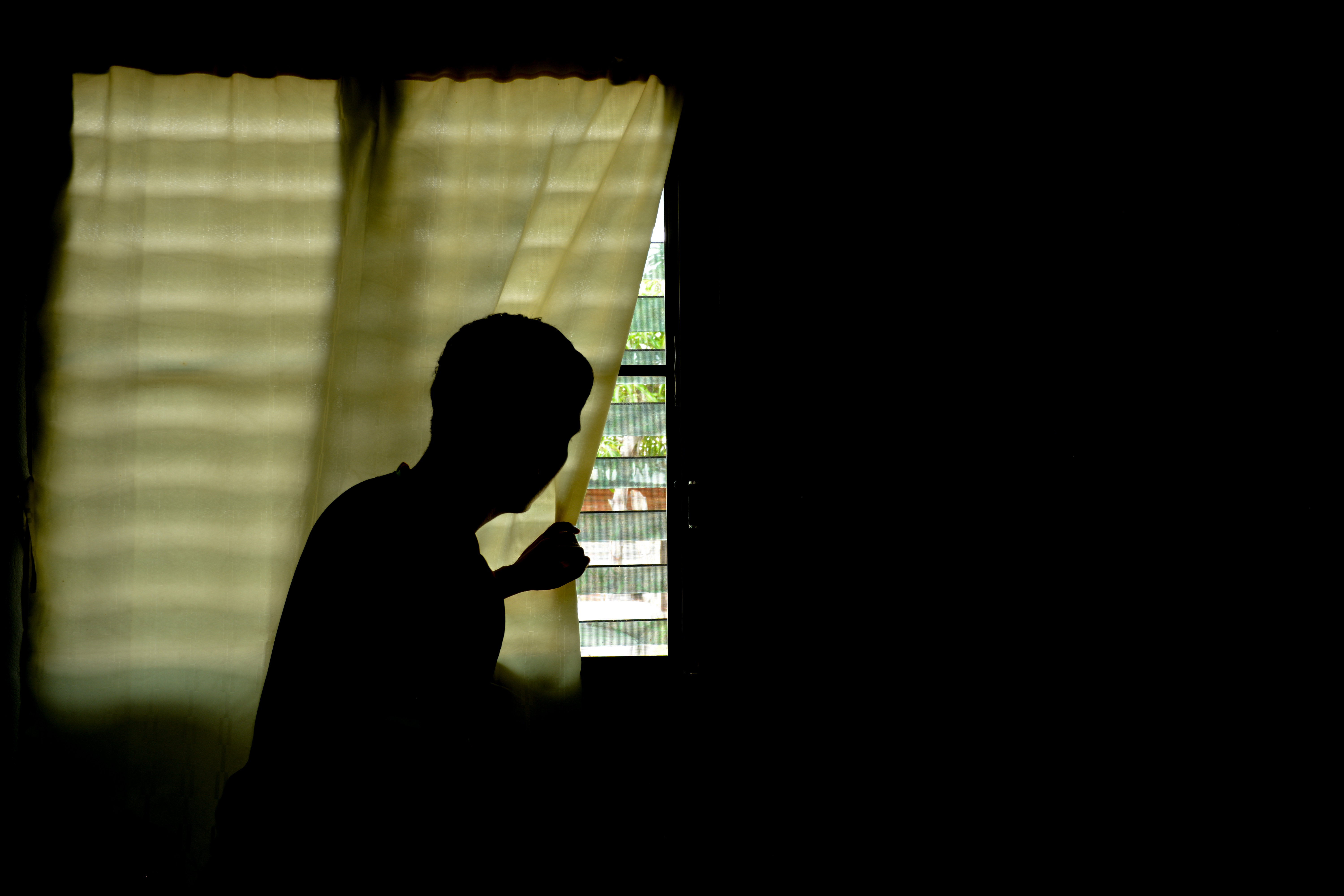 Silhouette man looking out the window with the light in the room. | Source: Shutterstock