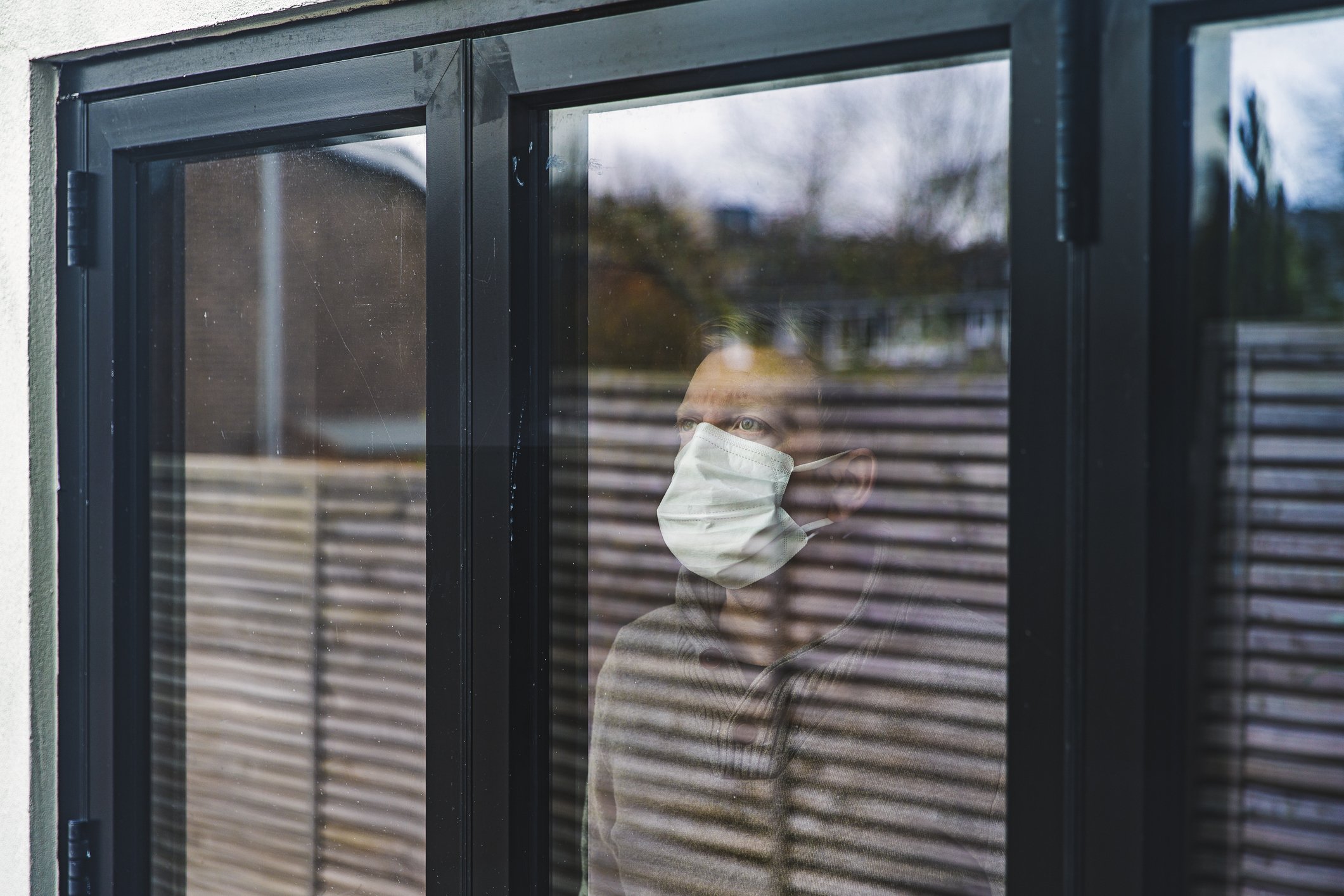 A photo of a man wearing protective mask and standing by the window. | Photo: Getty Images