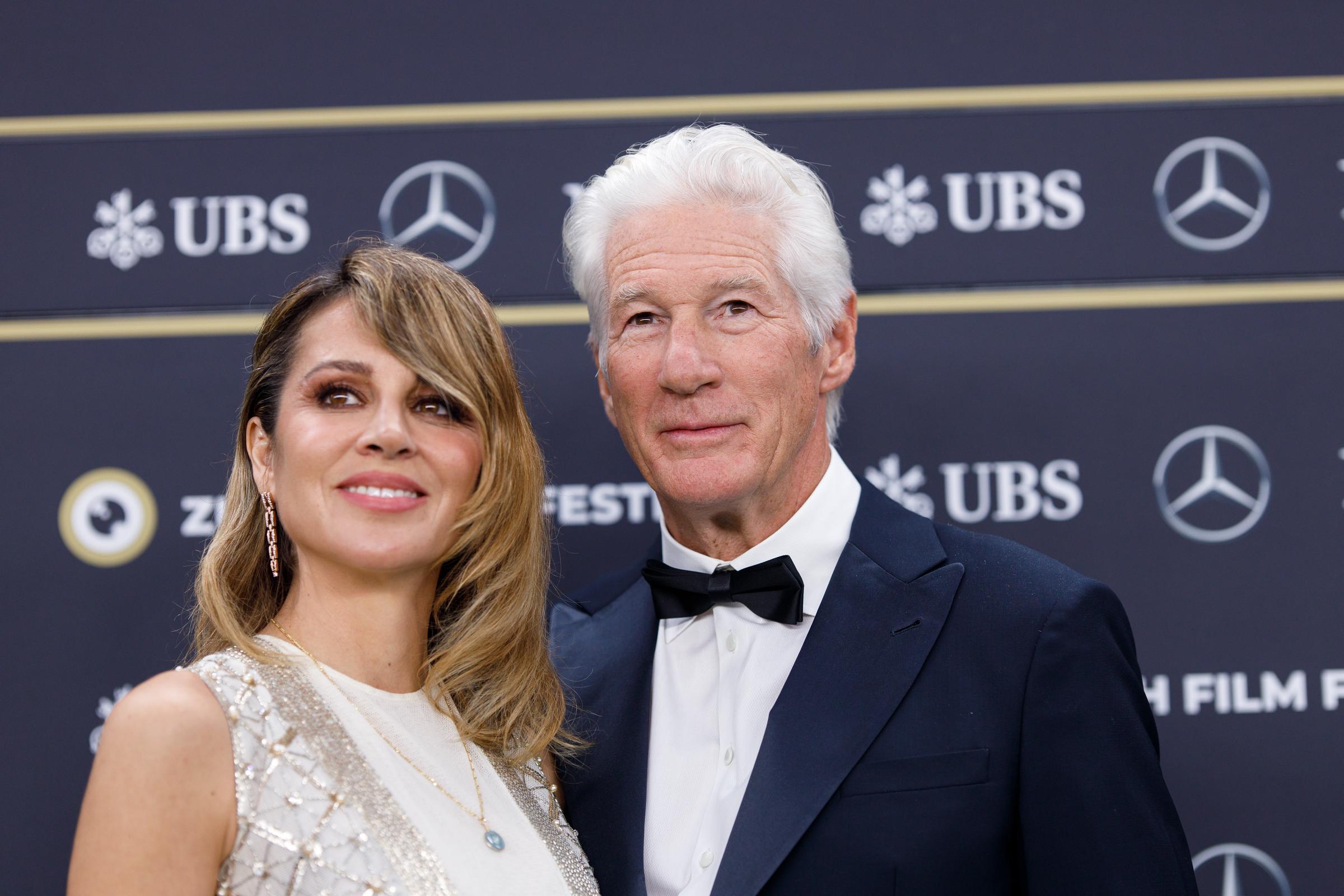 During the 20th Zurich Film Festival on October 8, 2024, Alejandra Gere and Richard Gere graced the “Wisdom of Happiness” green carpet — she radiant in an ivory cape gown, he refined in a tux — smiling beneath the evening glow of Zurich.
