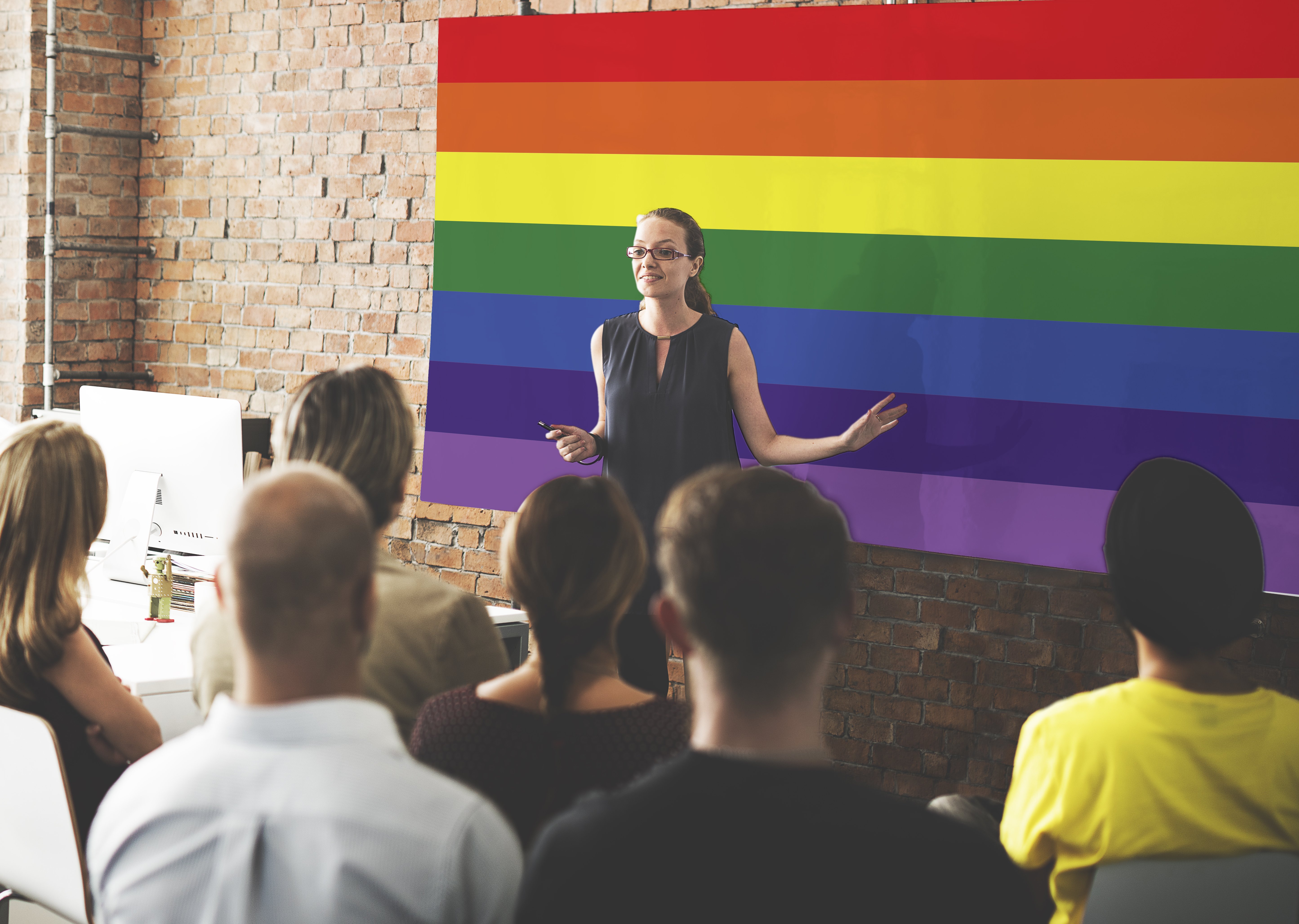 A teacher standing in front of a LGBTQ+ flag. | Source: Shutterstock 