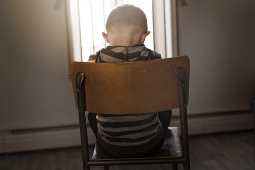 A sad child sitting on a chair in front of a window. | Source: Shutterstock.