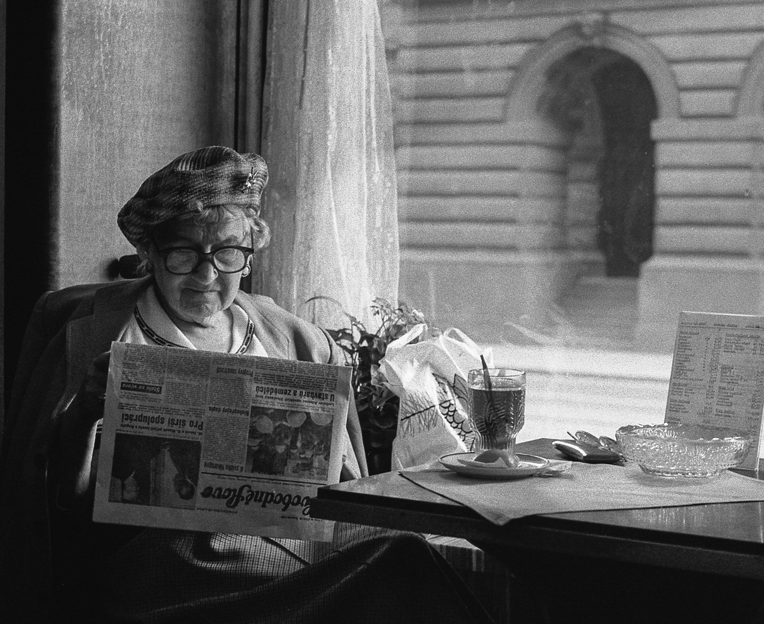 An older woman sitting an reading a newspaper while having a meal | Source: Unsplash