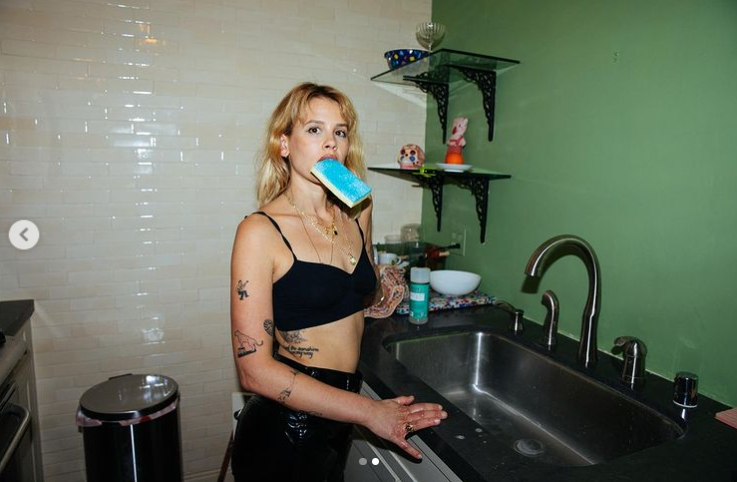 Sosie Bacon stands by the sink with a sponge in her mouth.| Source: Instagram/sosiebacon