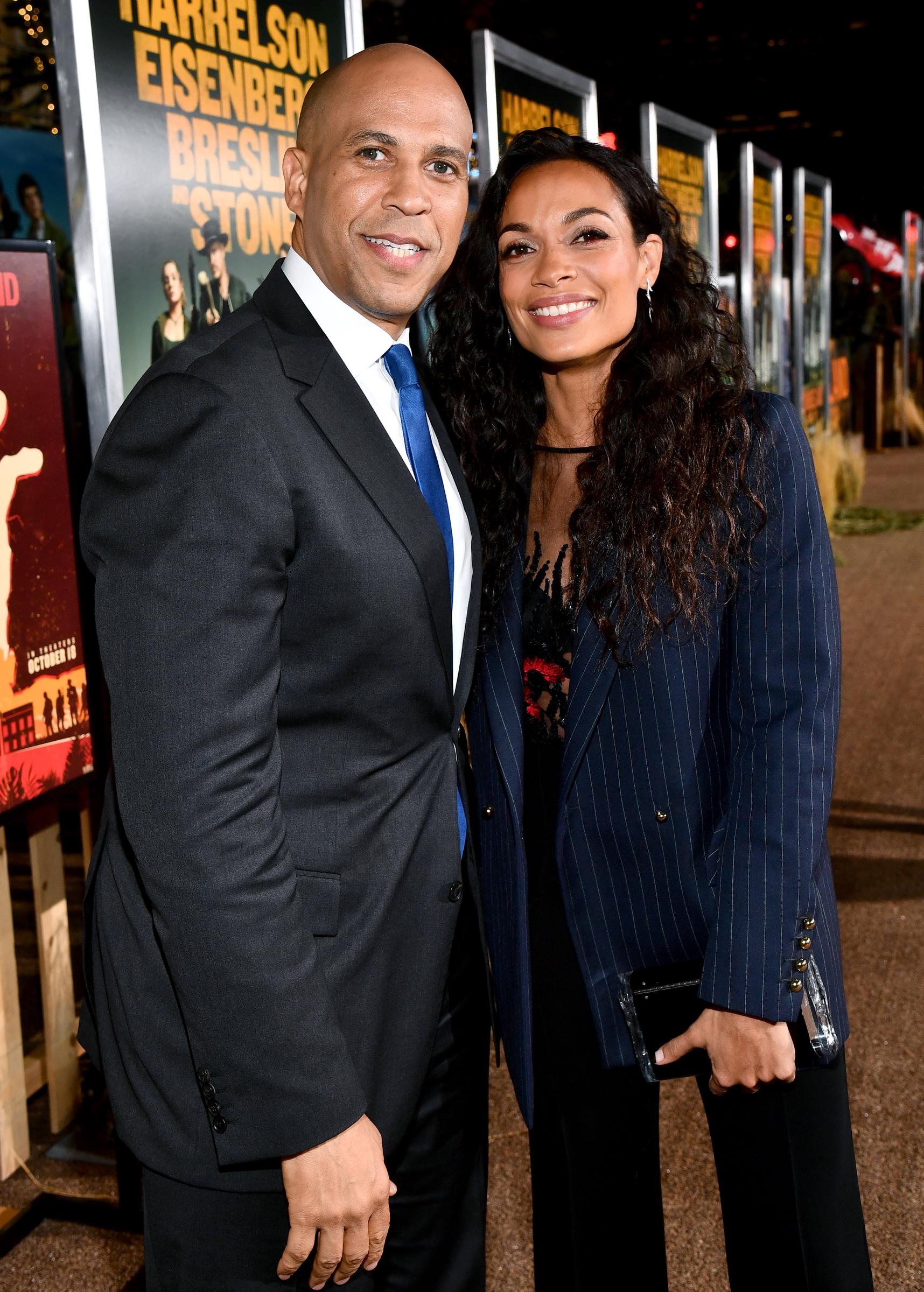 Cory Booker, dressed in a black suit, poses with Rosario Dawson, who stuns in a pinstripe blazer and flowing curls. Together, they strike a confident and stylish figure on the red carpet premiere for "Jay and Silent Bob Reboot."