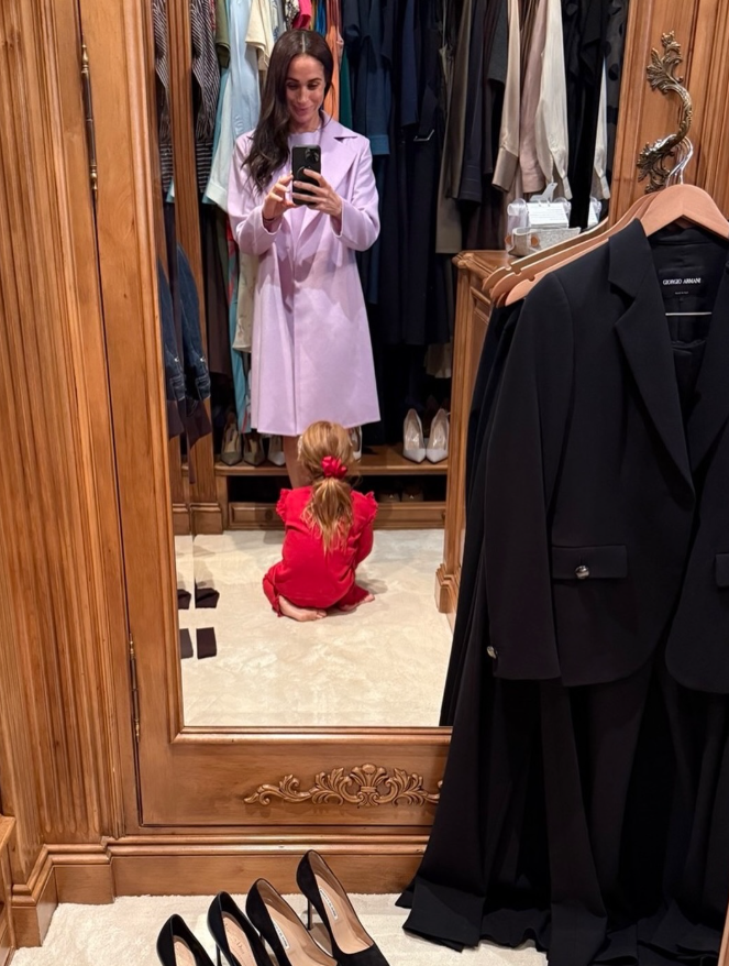 Meghan Markle smiles while taking a mirror selfie as Princess Lilibet sits on the floor of a walk-in closet dressed in a bright red outfit. | Source: Instagram/meghan