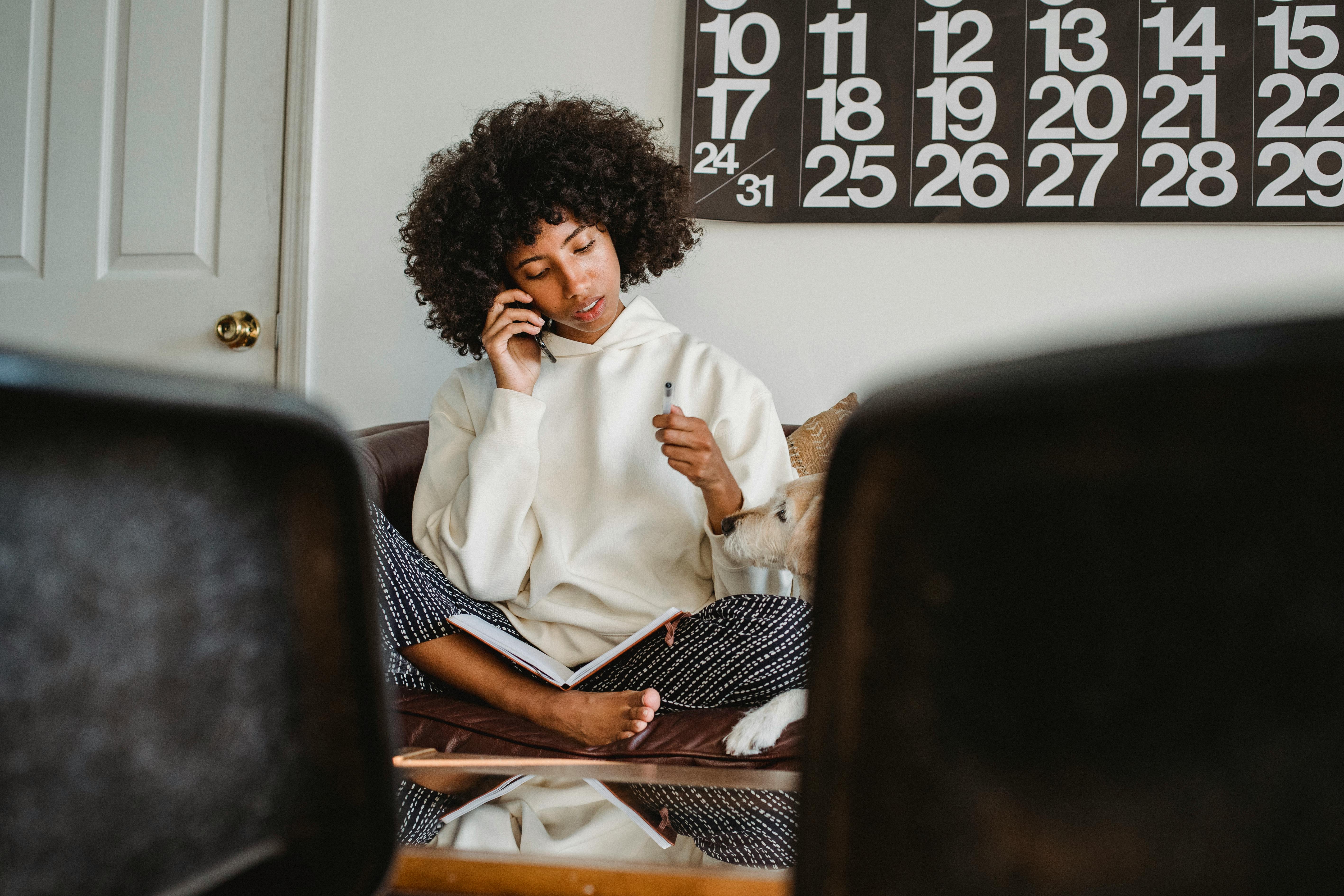 An unhappy woman talking on a phone while sitting with a notebook | Source: Pexels