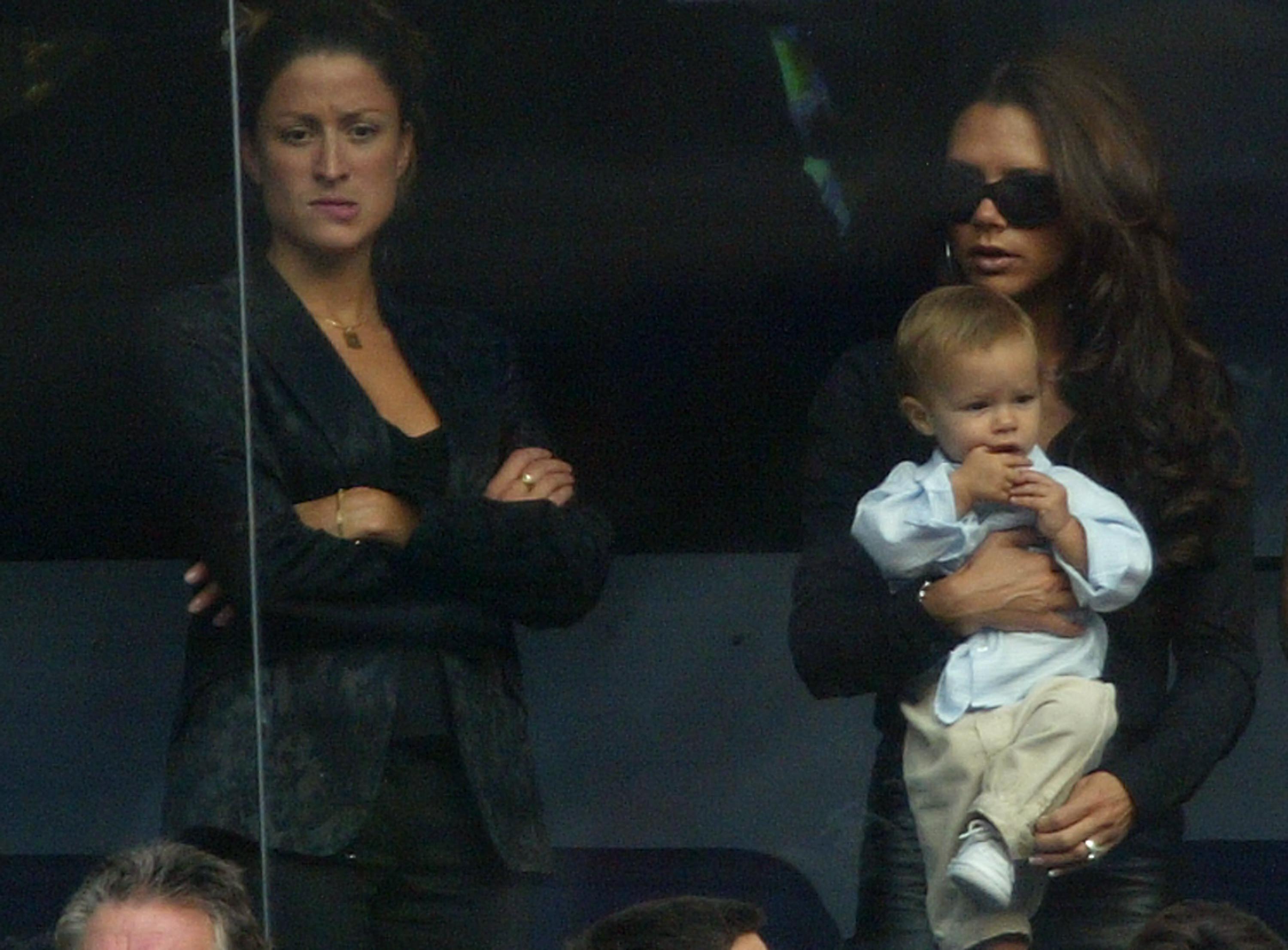 Rebecca Loos stands beside Victoria Beckham carrying her son Romeo during the Spanish Primera Liga match between Real Madrid and Valladolid at the Santiago Bernabeu Stadium on September 13, 2003 in Madrid, Spain. | Source: Getty Images