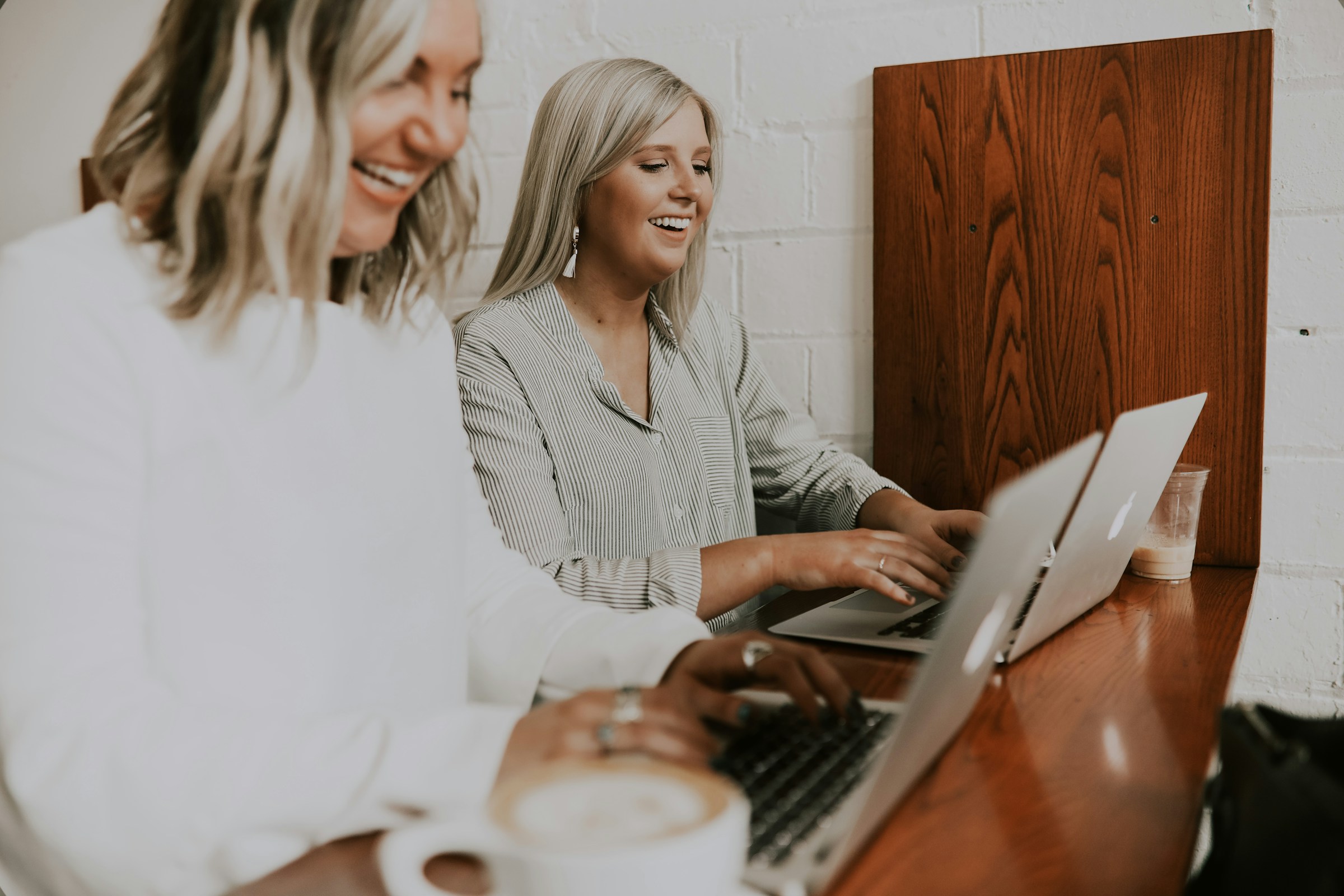 Dos mujeres riéndose mientras usan sus computadoras portátiles en una oficina | Fuente: Unsplash