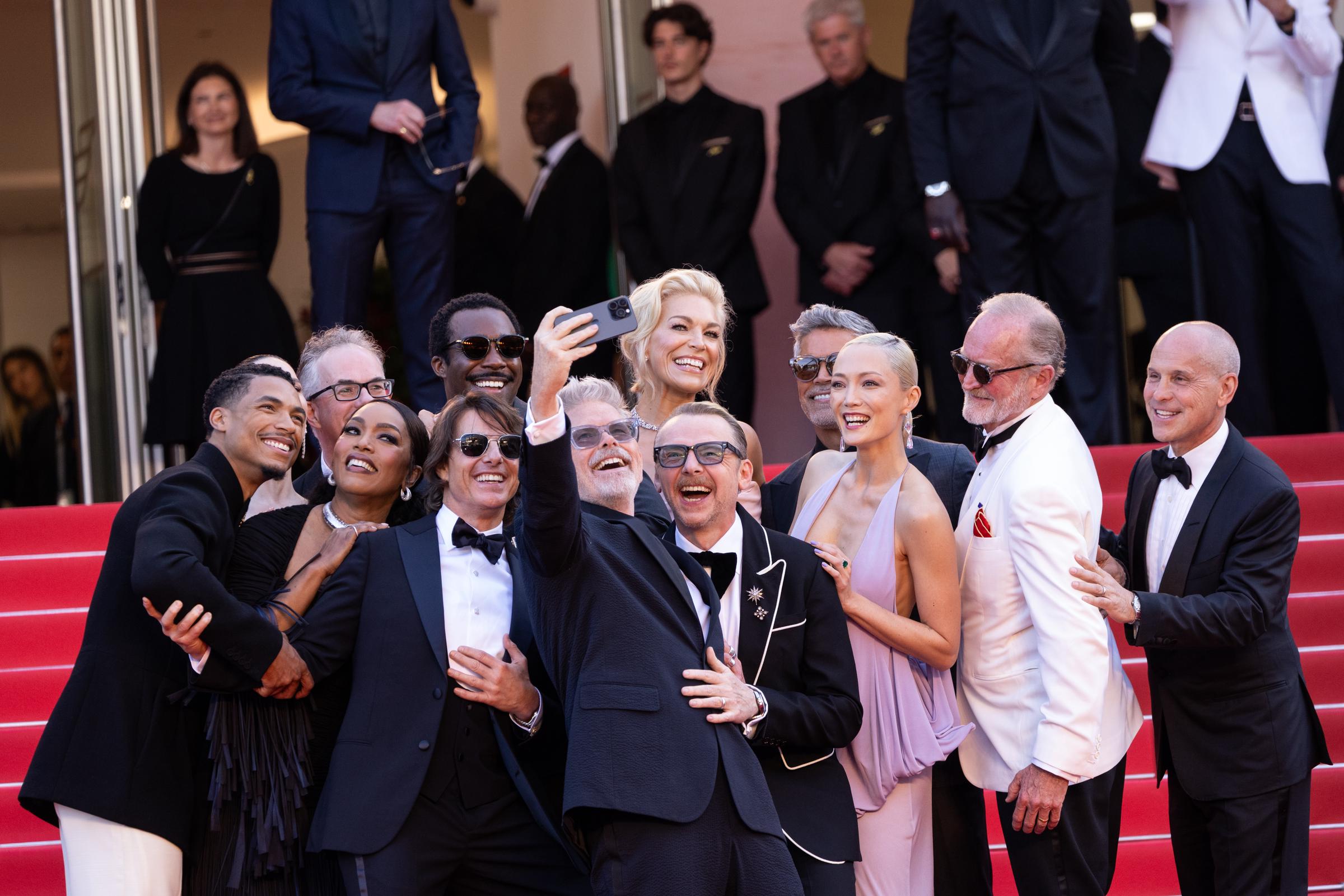 Tom Cruise joins co-stars and filmmakers for a cheerful group selfie on the red carpet at the "Mission: Impossible – The Final Reckoning" premiere during the 78th Cannes Film Festival. The cast shares a lighthearted moment before the evening screening.